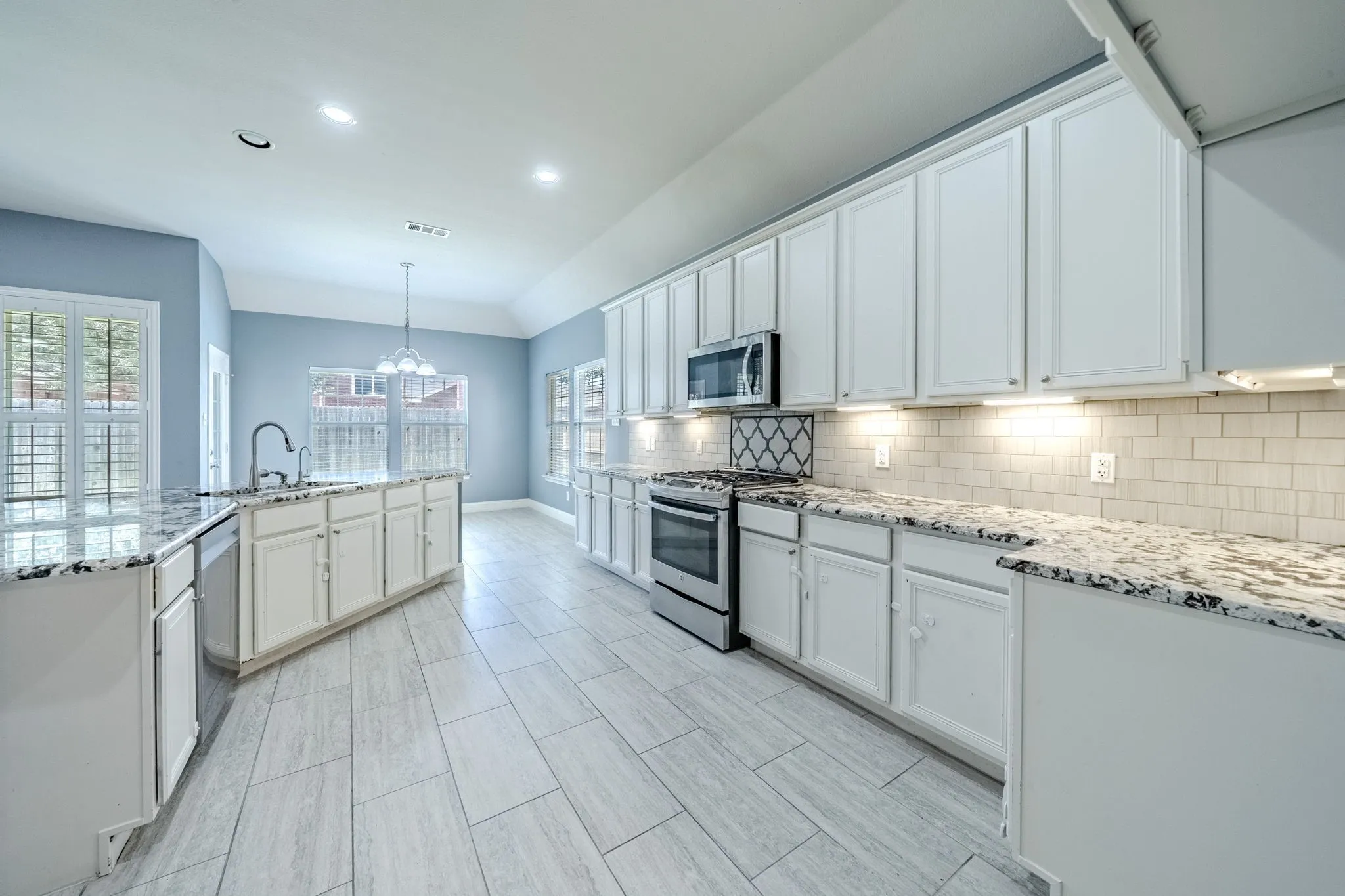 Contemporary kitchen featuring extensive white cabinetry, granite countertops, stainless steel appliances, and a tiled backsplash