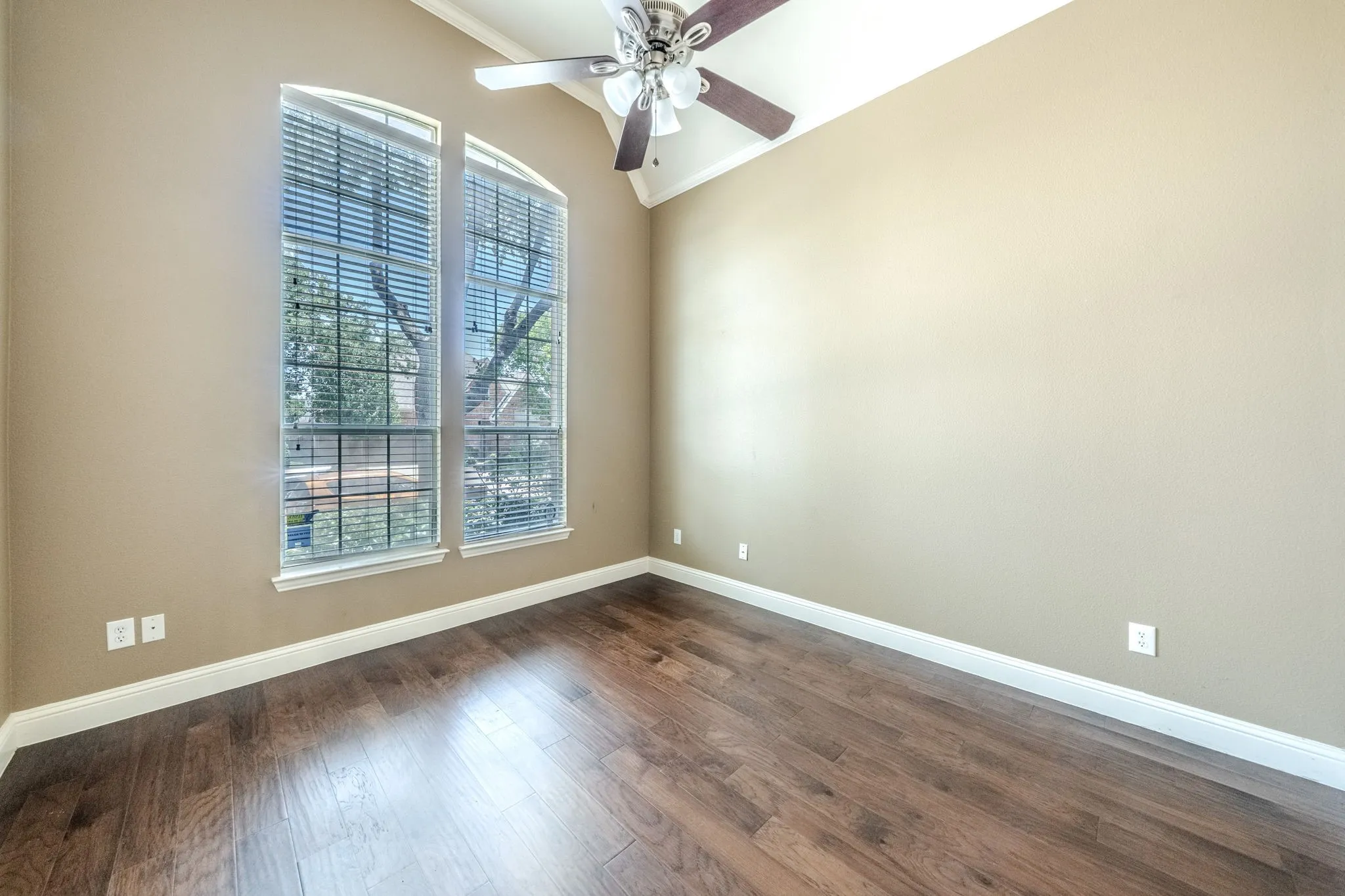 Vaulted ceiling room featuring twin arched windows with blinds, wood-finish flooring, and a ceiling fan