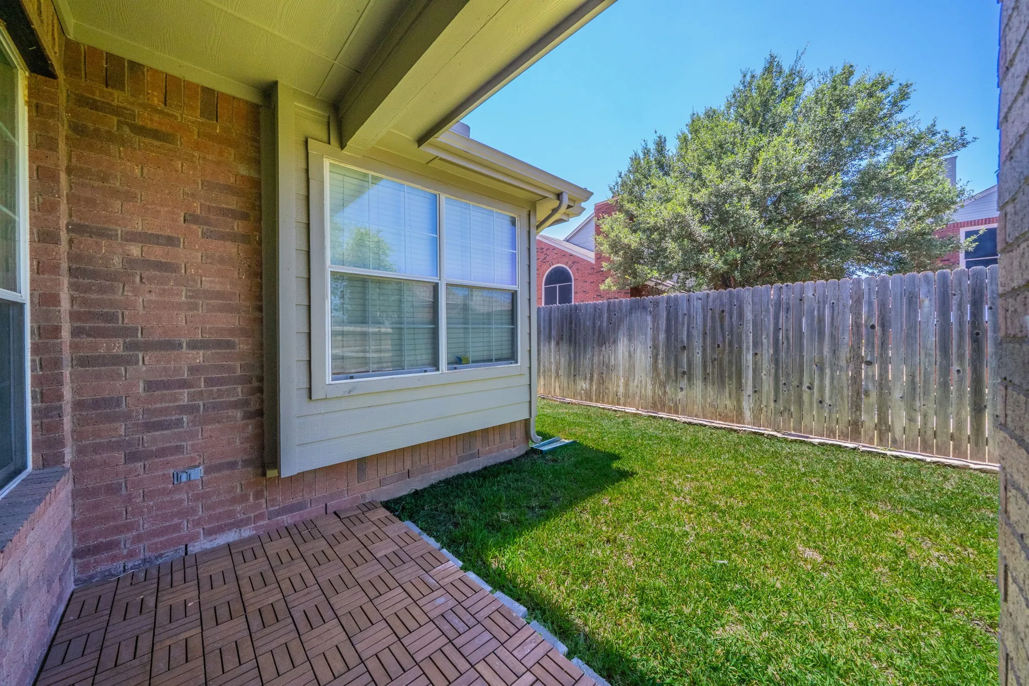 Covered patio featuring wood-finish tile flooring, brick exterior, and a privacy fence