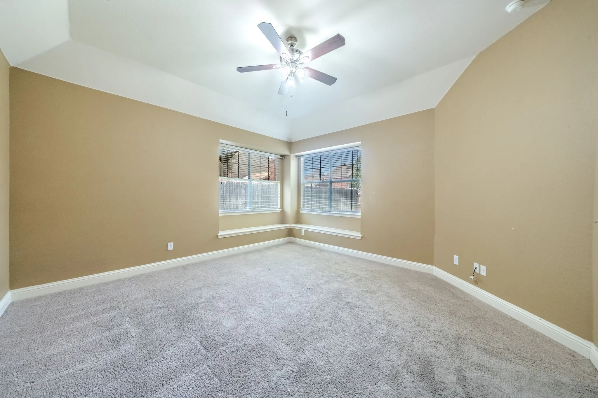 Spacious room featuring vaulted ceilings, a ceiling fan with integrated lighting, and light-toned carpeting