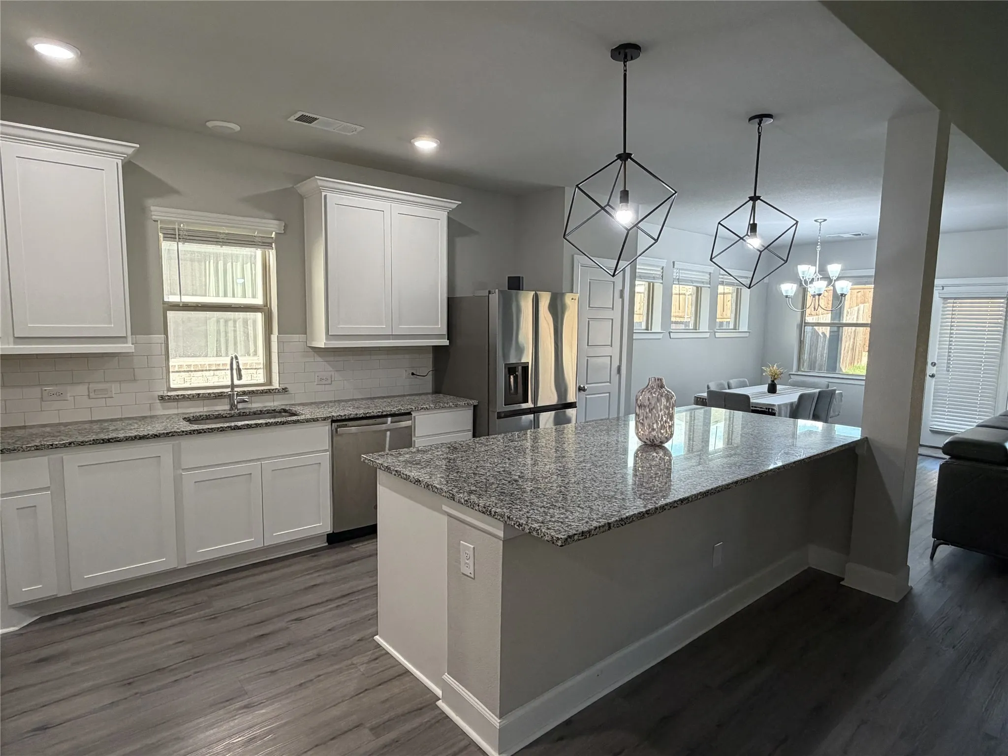 Spacious kitchen featuring an island with a granite countertop, white shaker cabinetry, stainless steel appliances, wood-finish flooring, and subway tile backsplash