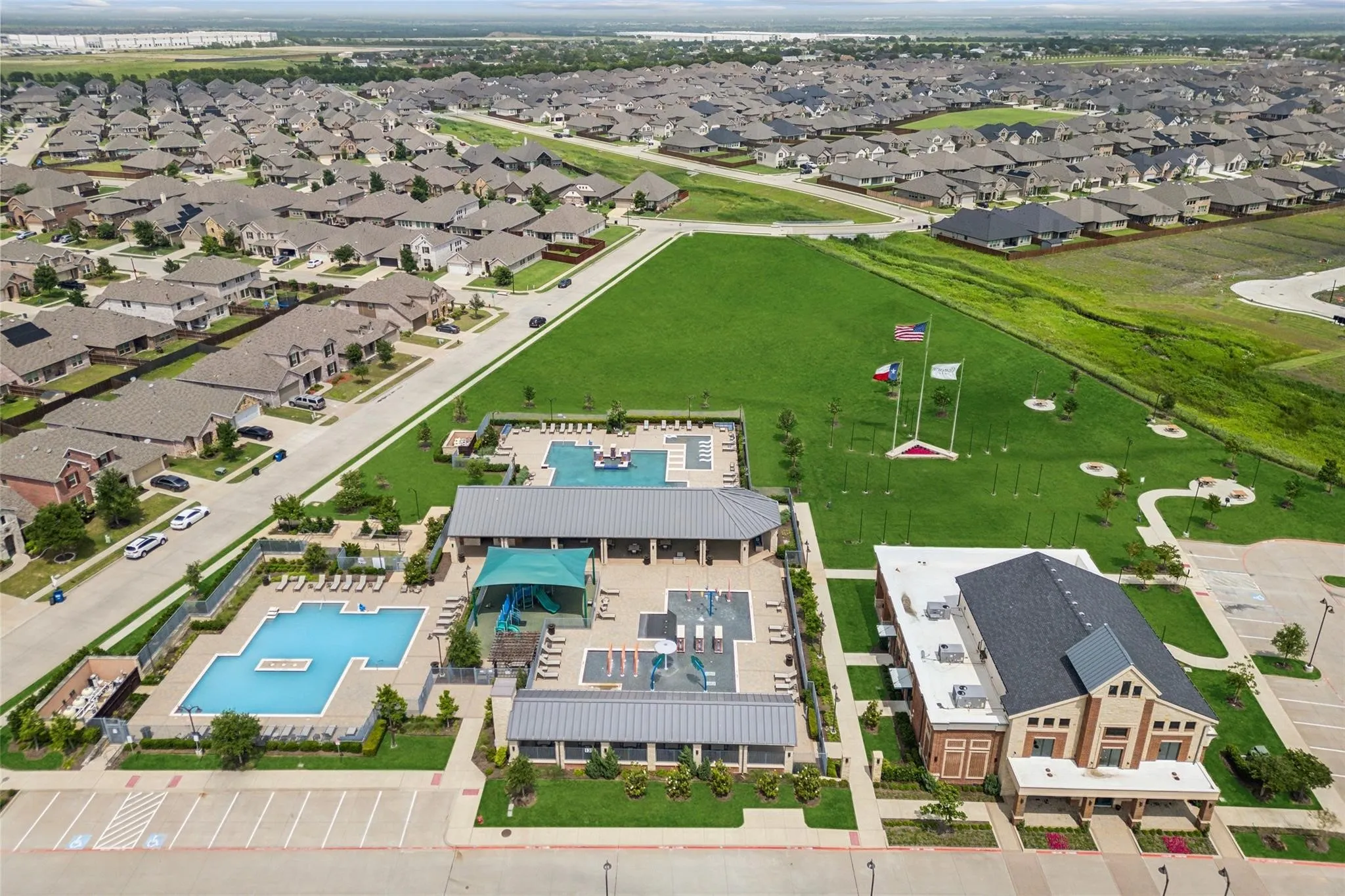 Community amenity center featuring multiple swimming pools with surrounding lounge areas, a covered playground, and an adjacent clubhouse building