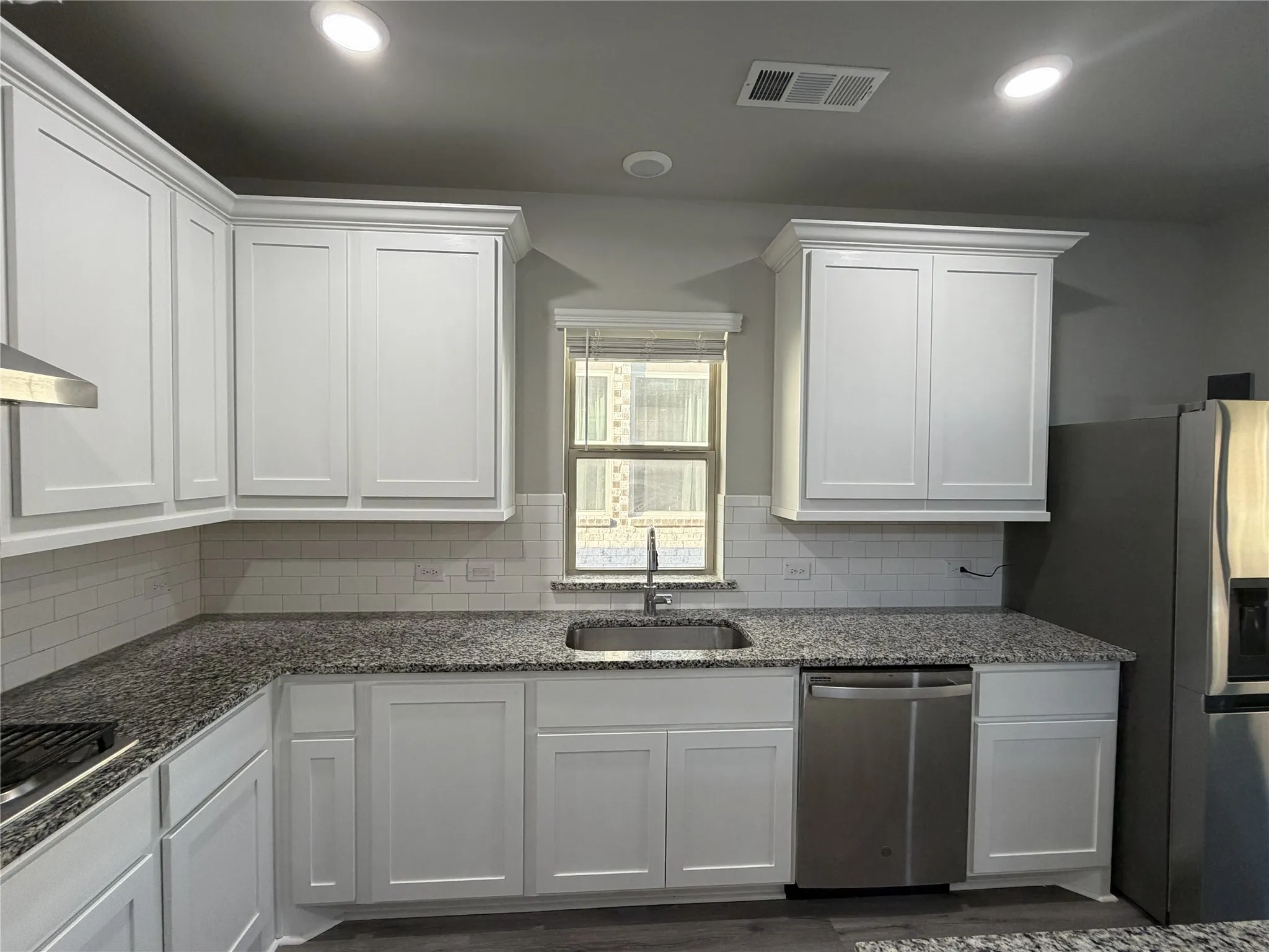 Kitchen featuring white shaker-style cabinetry with crown molding, speckled countertops, a stainless steel dishwasher, and subway tile backsplash
