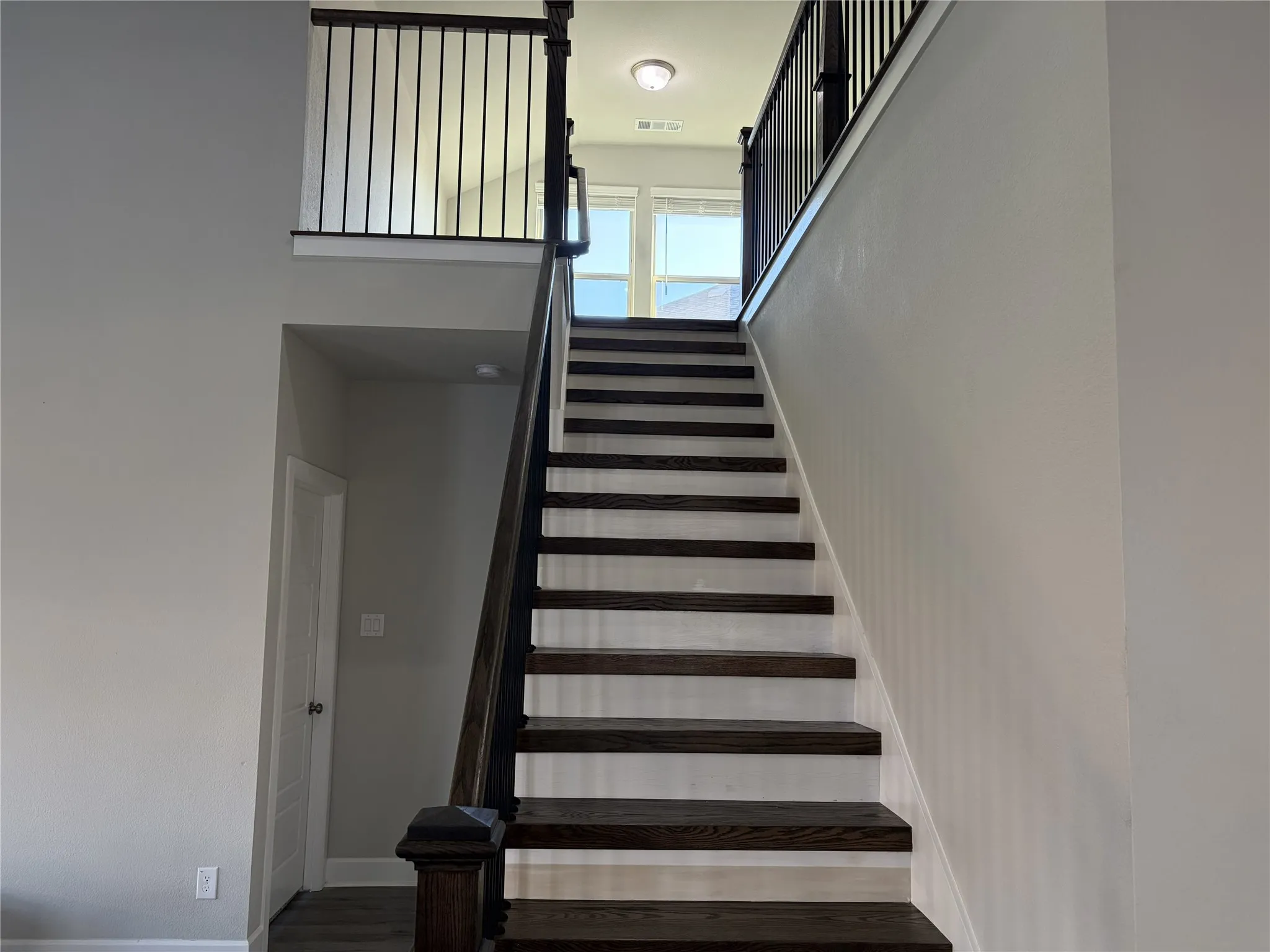 Staircase featuring dark wood-finish treads and risers, black metal balusters, and a dark wood-finish handrail