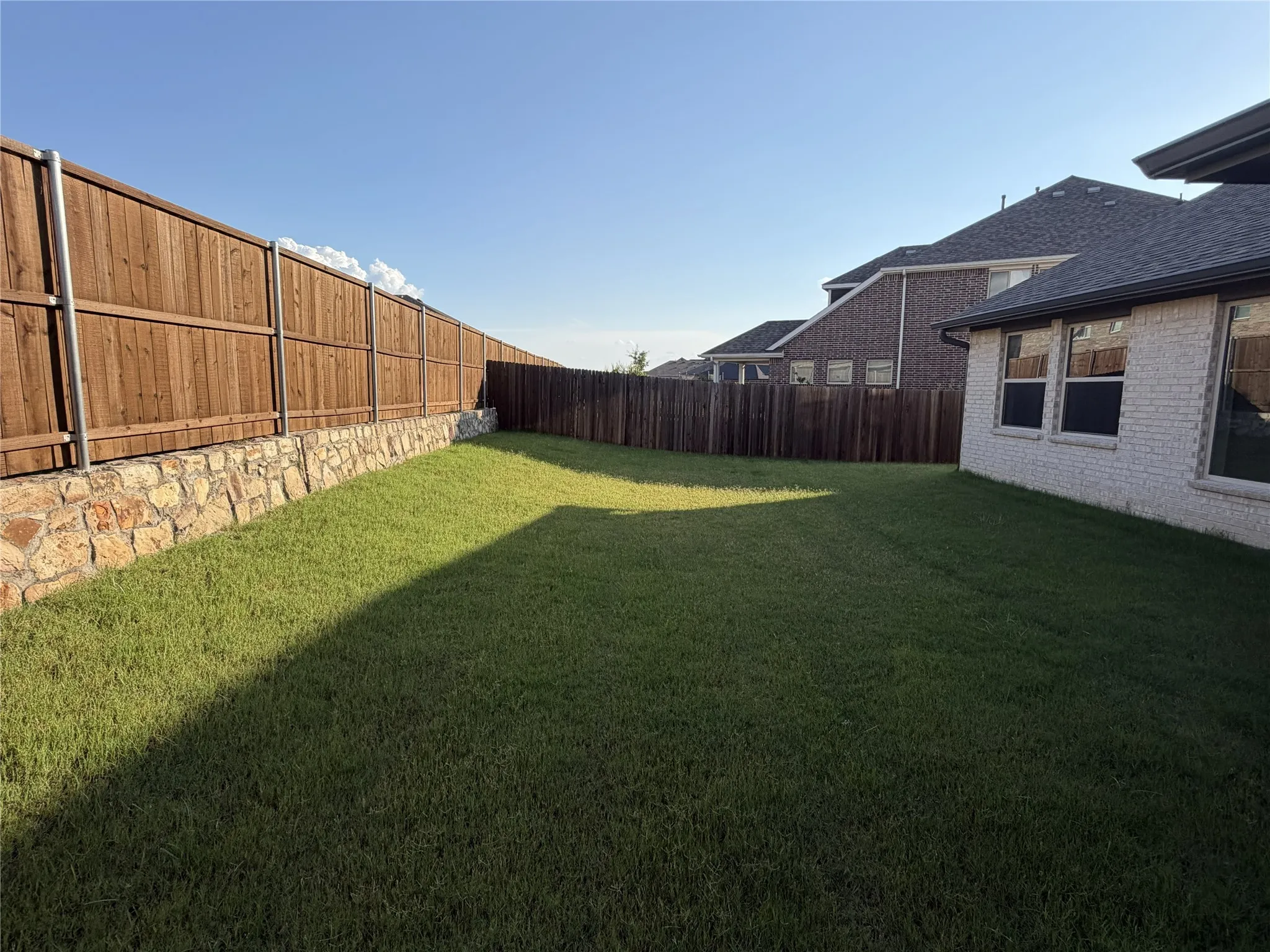 Expansive lawn area with a multi-level wood privacy fence, featuring a stone retaining wall
