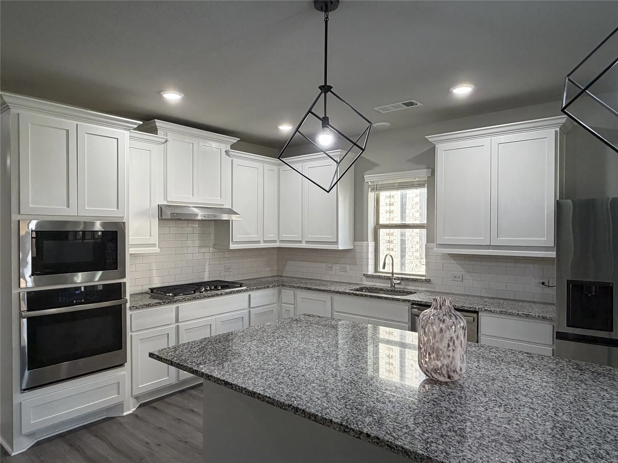 Kitchen featuring white shaker cabinetry, granite countertops, stainless steel appliances, a subway tile backsplash, and wood-finish flooring