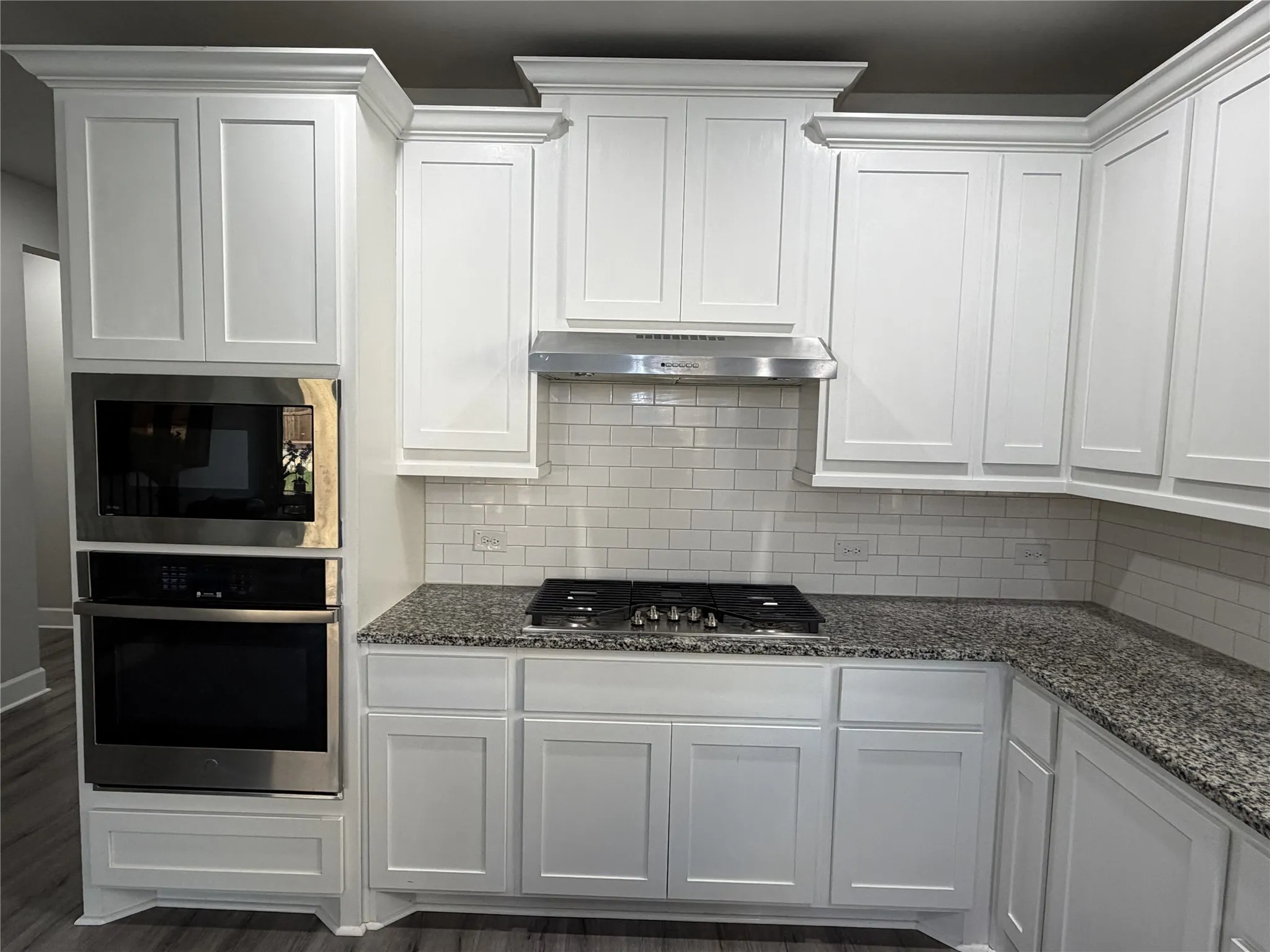 Modern kitchen featuring white shaker cabinetry with crown molding, stainless steel built-in microwave and oven, a gas cooktop, subway tile backsplash, and speckled countertops