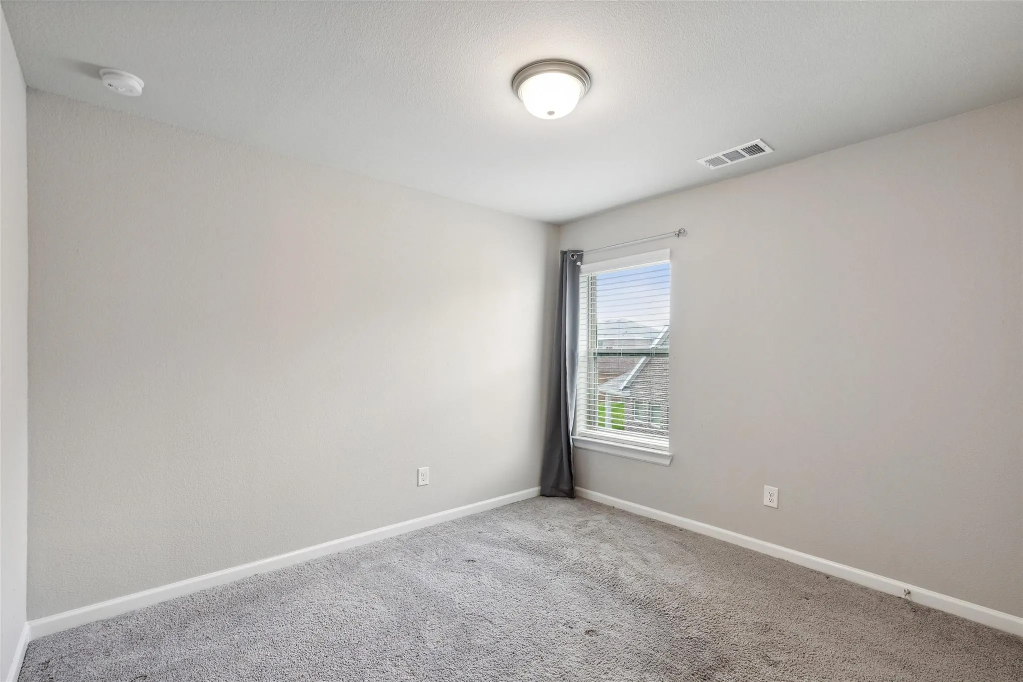 2nd Floor Bedroom 2 - Light-filled room featuring soft gray walls, a single window with blinds, and gray carpet flooring