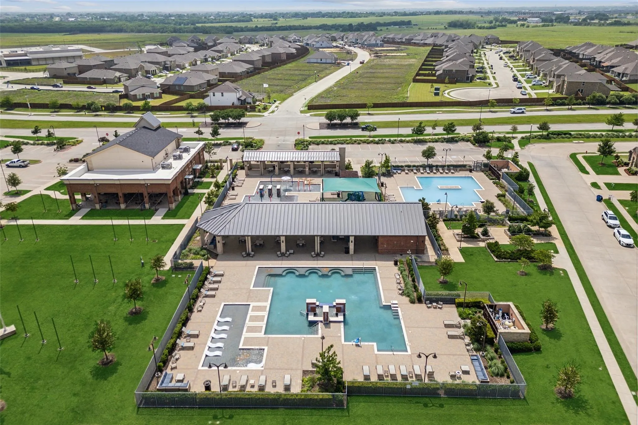 Community recreation center featuring multiple pools, expansive green spaces, and shaded lounge areas