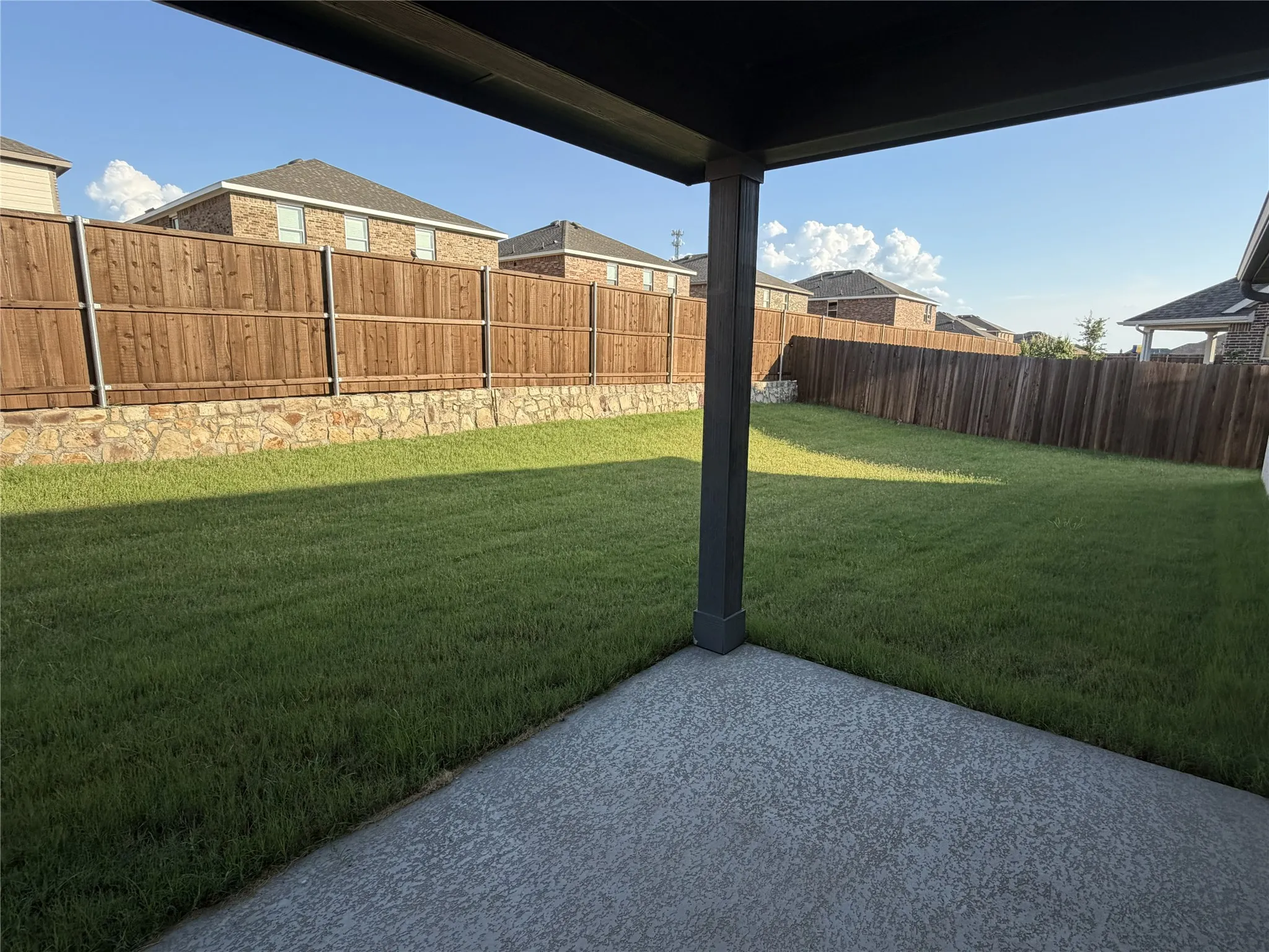 Covered patio with a textured concrete surface, overlooking a spacious lawn