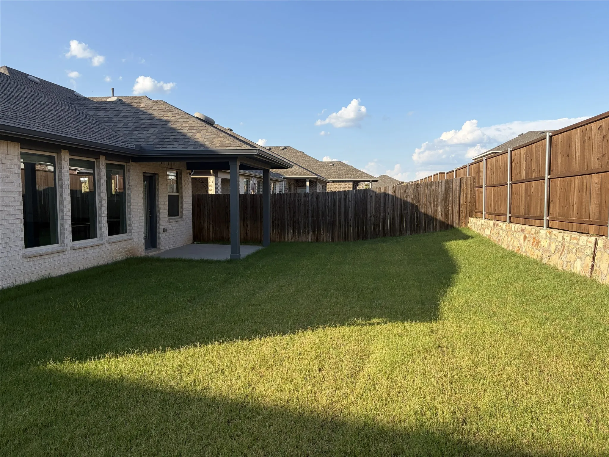 Spacious backyard featuring a covered patio with concrete flooring, a large grassy area, and a wood privacy fence