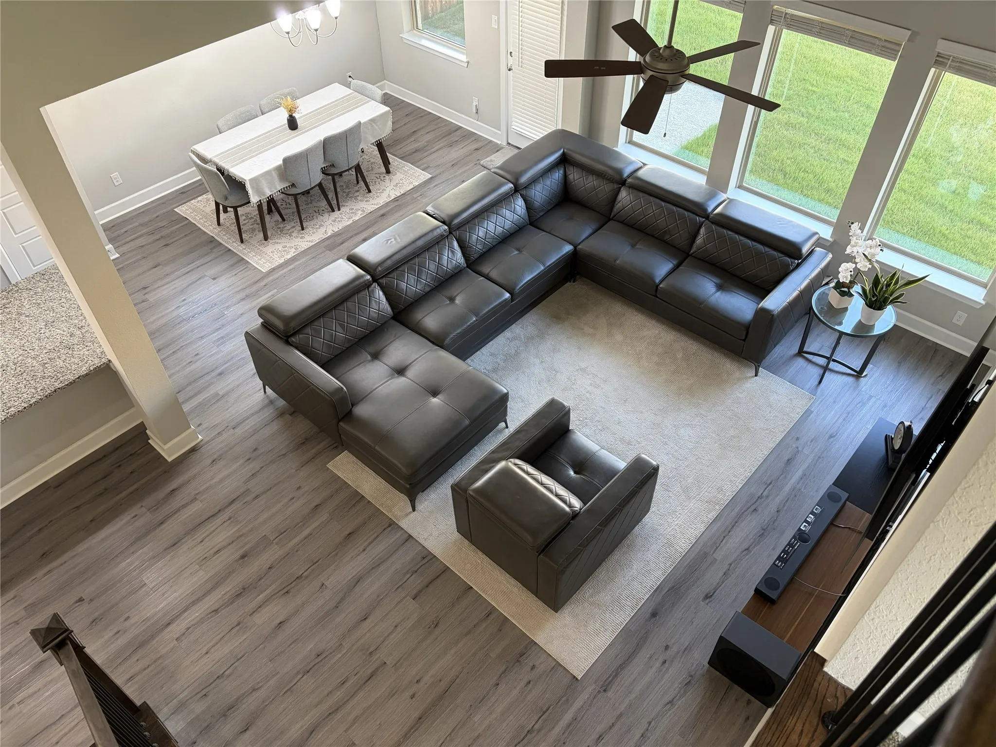 Open-concept living area featuring wood-finish flooring, a contemporary chandelier, large windows providing abundant natural light, a ceiling fan, and a dining space