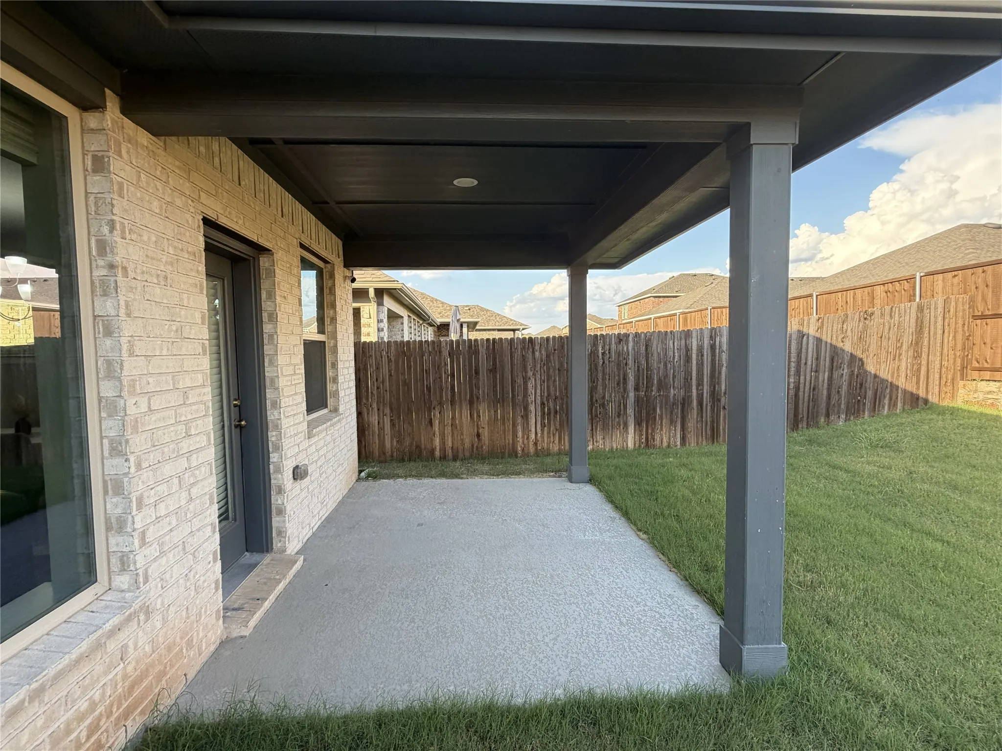 Expansive covered patio featuring a concrete surface, gray support columns, and a dark ceiling with recessed lighting