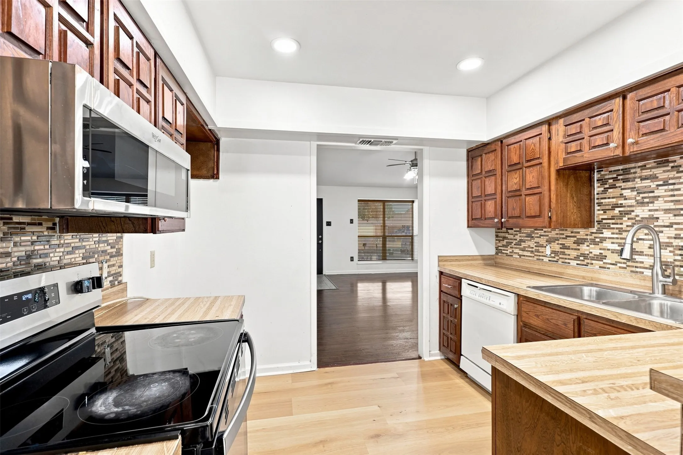 Kitchen featuring wood cabinetry, stainless steel microwave, tile backsplash, laminate countertops, and wood-finish flooring
