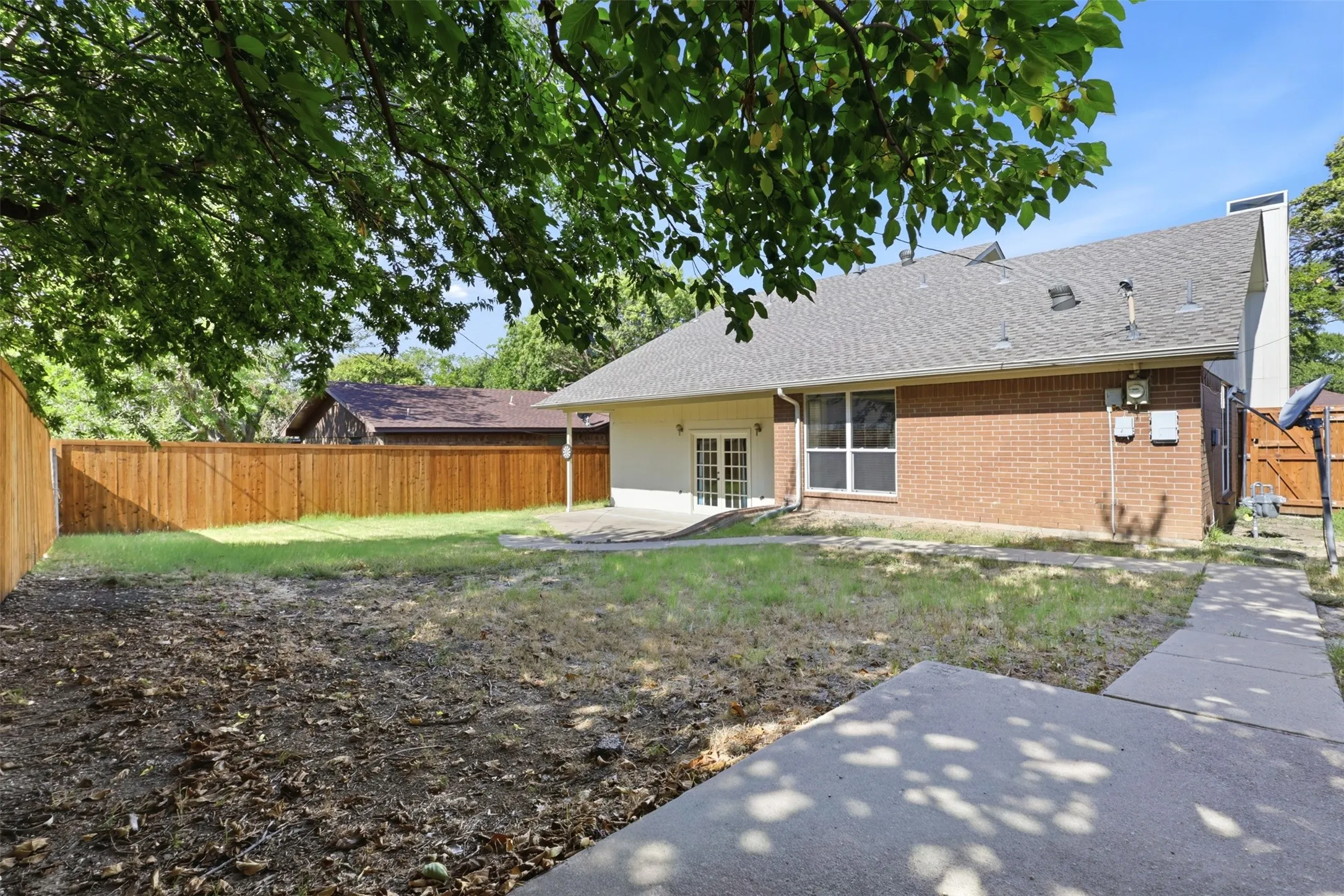 Expansive backyard with a wood privacy fence, concrete patio, and mature trees