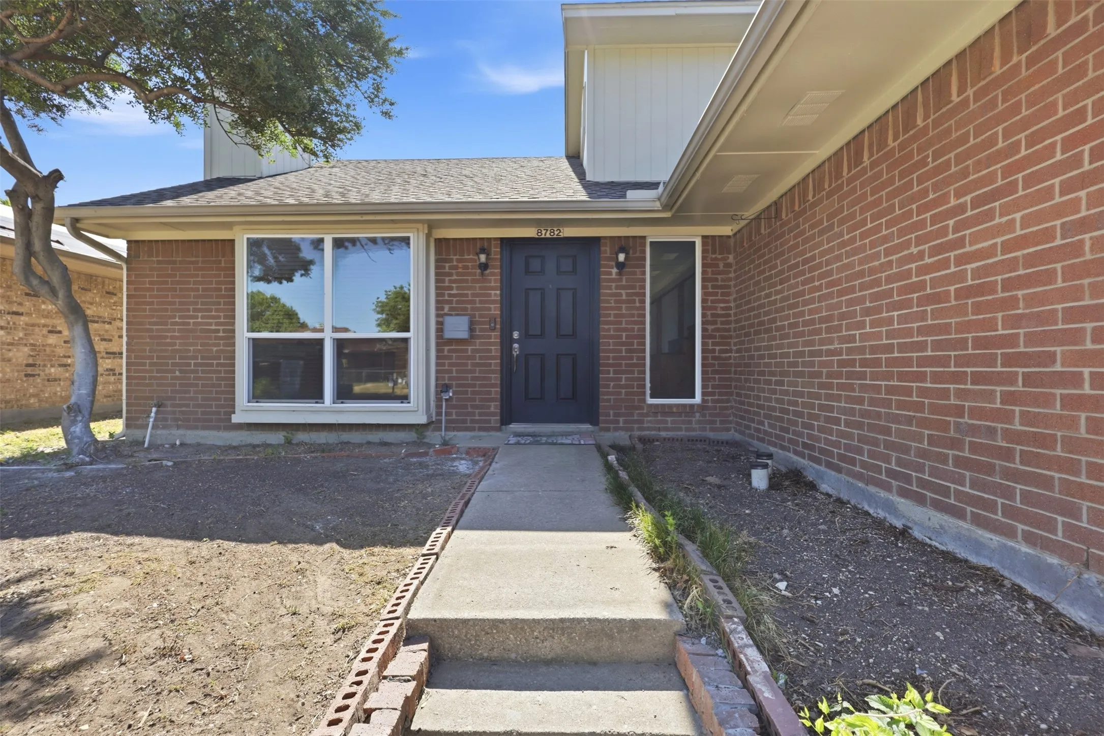 Brick exterior with a dark-paneled entry door, concrete walkway, and a prominent front window