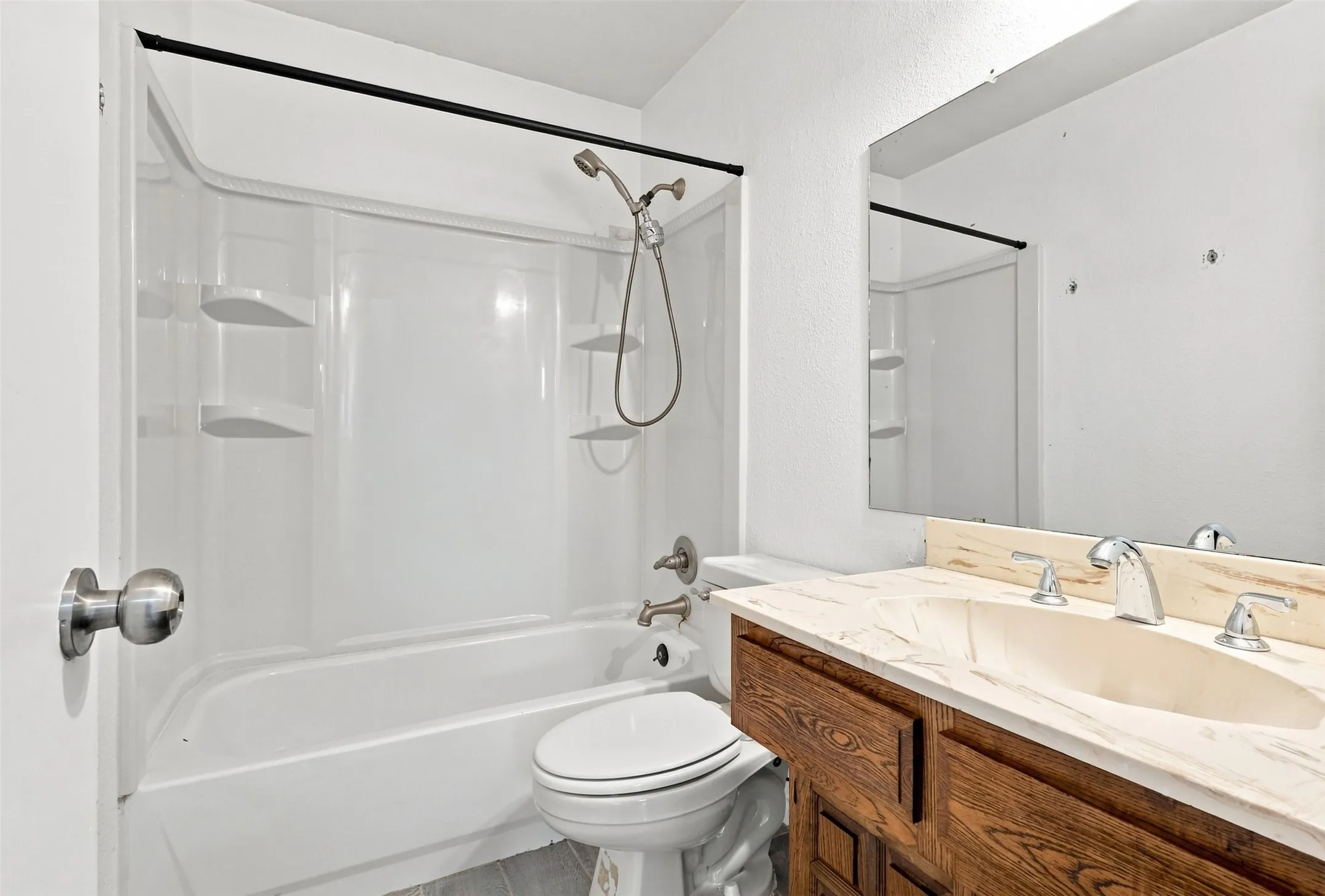 Integrated bathtub and shower combination with chrome fixtures, vanity with wood-finish cabinetry, and a countertop with integrated sink