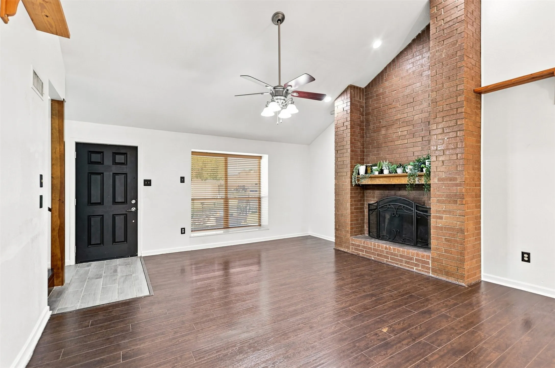 Vaulted ceilings, wood-finish flooring, and a brick-finish fireplace with a built-in mantel