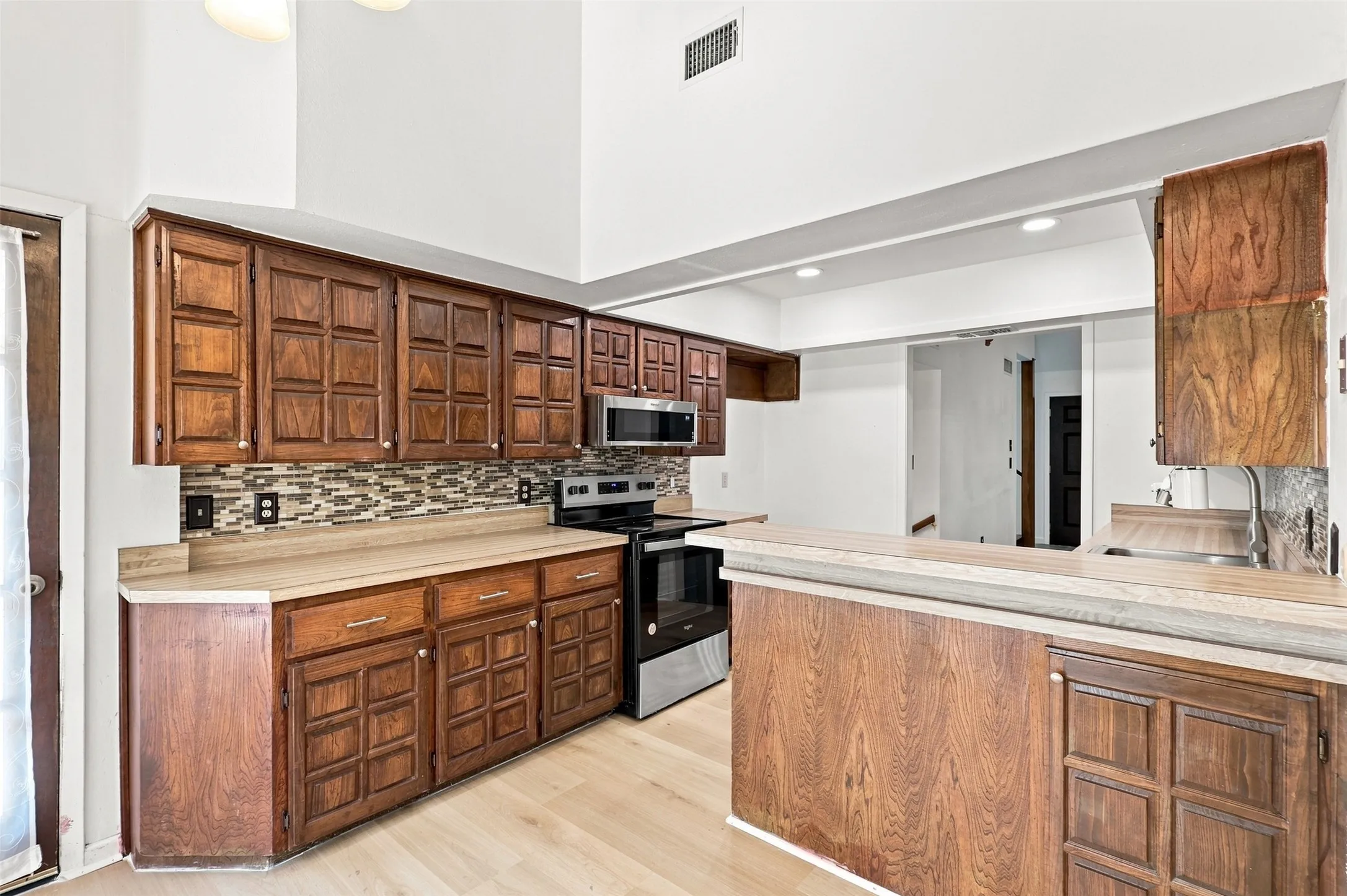 Vaulted ceilings, wood-finish cabinetry, tile backsplash, stainless steel appliances, and light wood-finish flooring