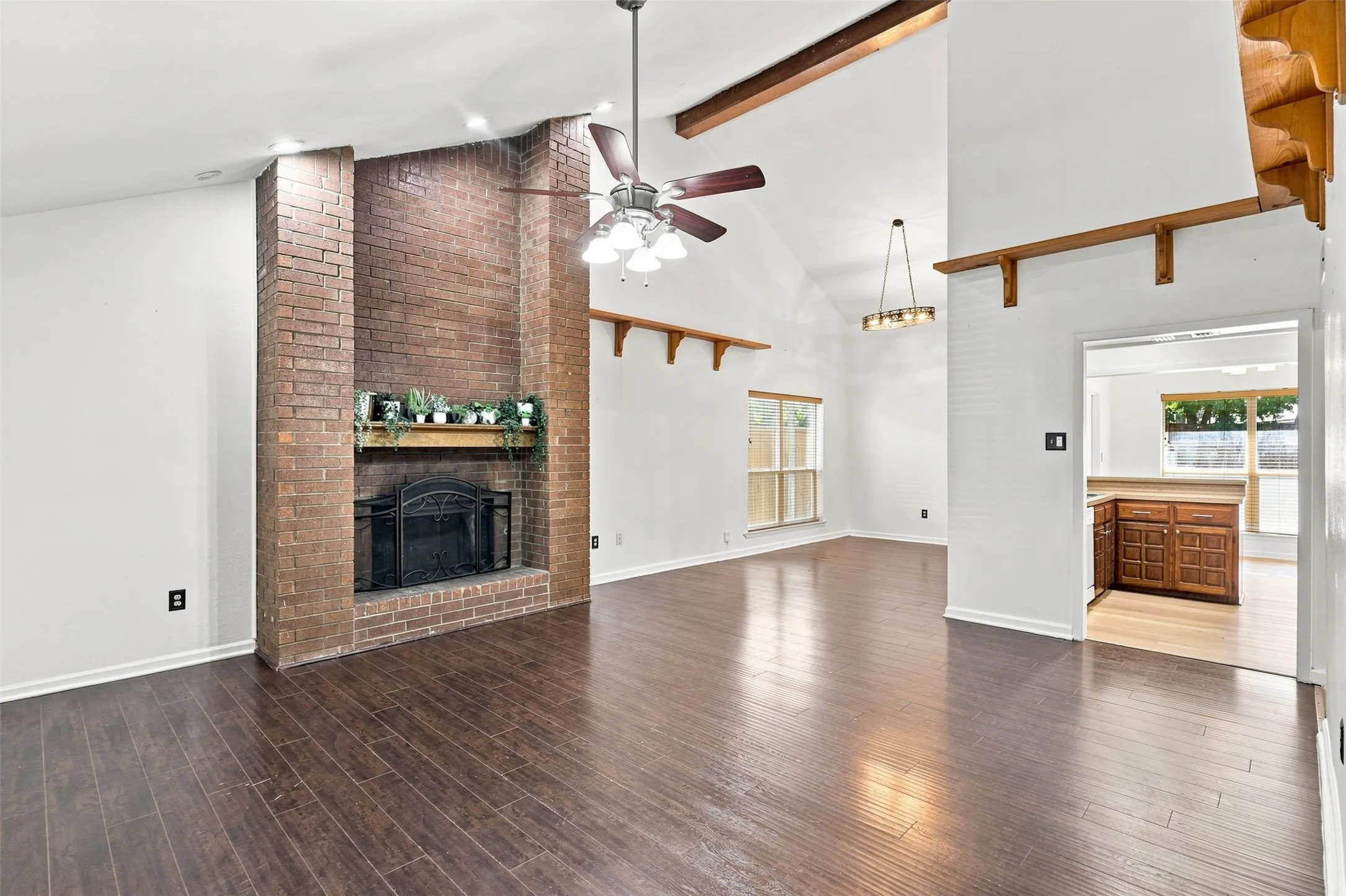Vaulted ceilings with exposed wood beams, brick fireplace with mantel, wood-finish flooring, and recessed lighting