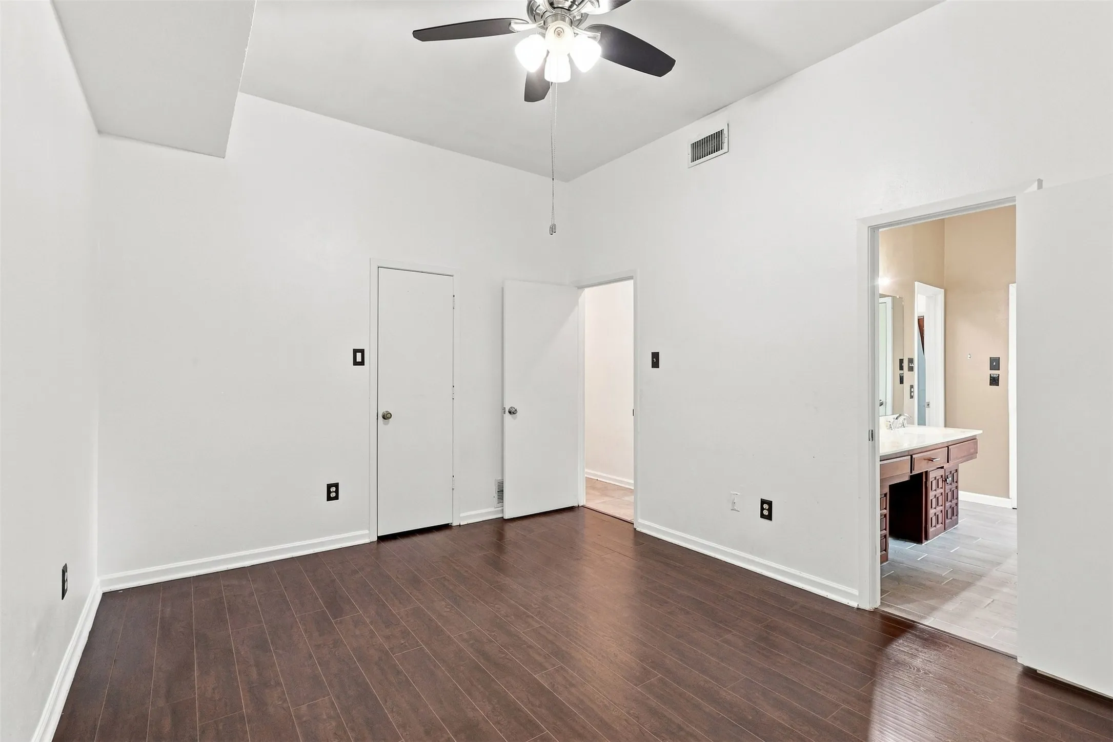 Vaulted ceiling with a ceiling fan, dark wood-finish flooring, and white walls