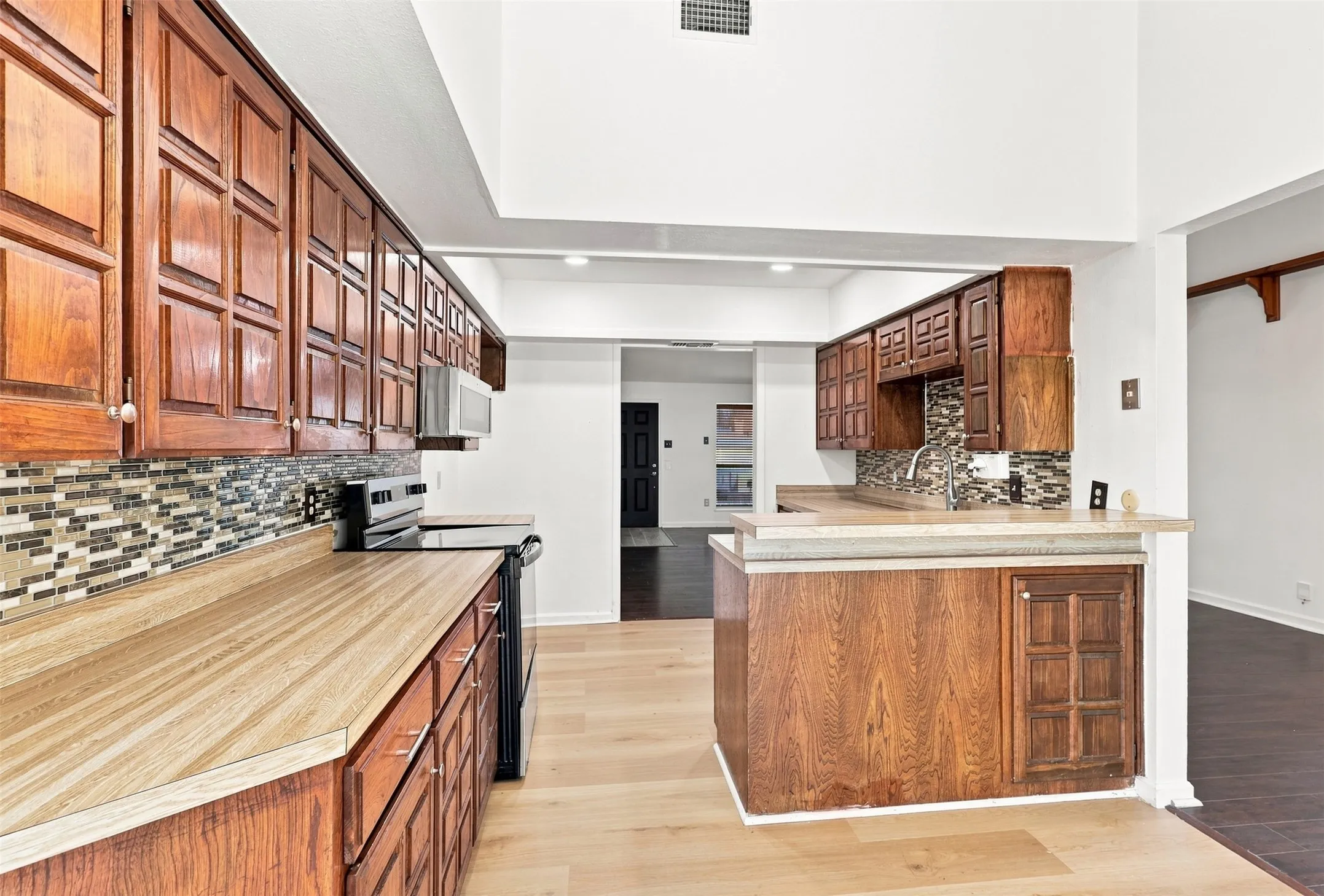 Kitchen featuring wood cabinetry, an integrated microwave, a tile backsplash, and a contemporary sink with a faucet