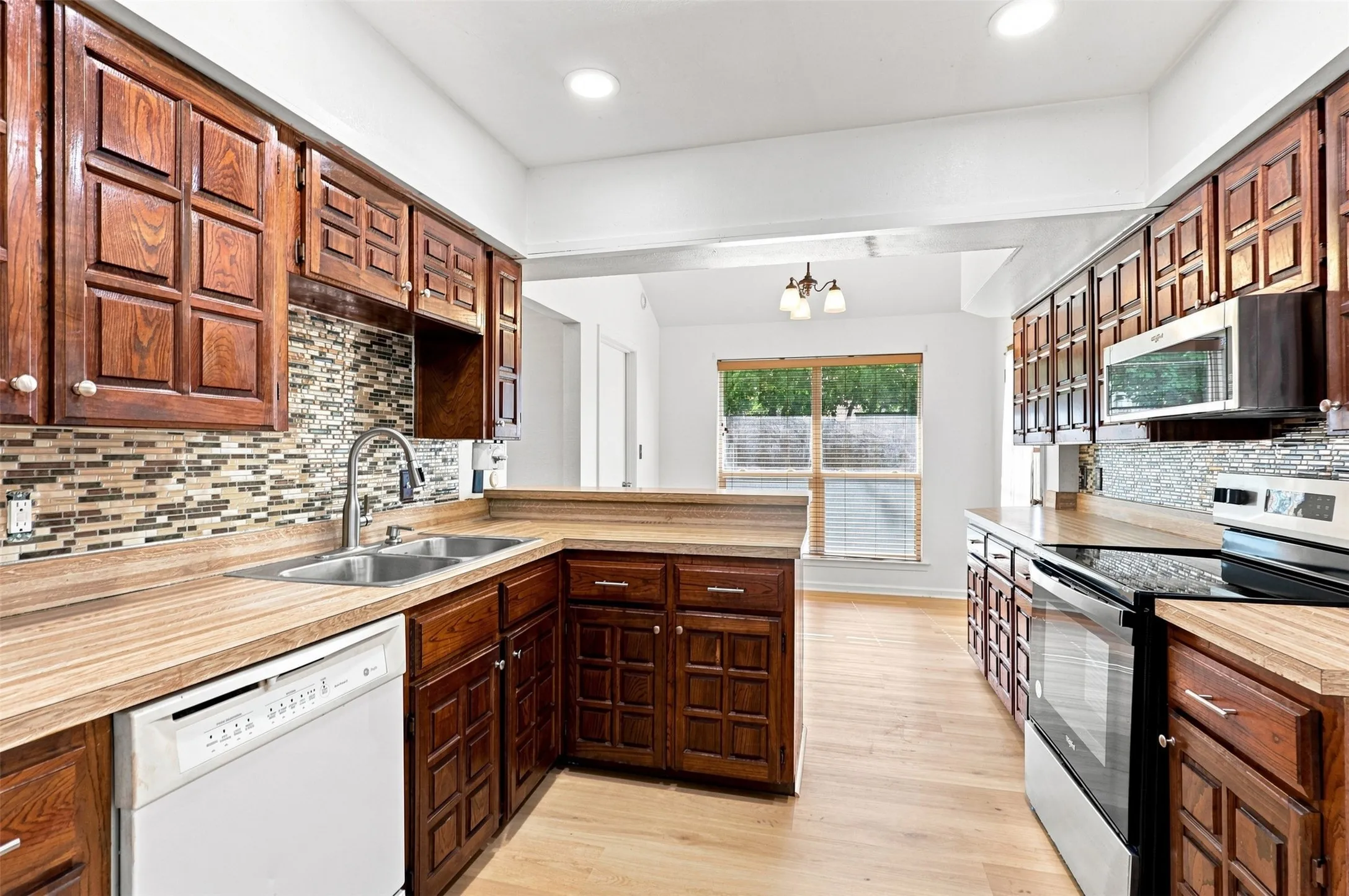 Kitchen featuring wood-finish flooring, wood cabinetry, stainless steel appliances, mosaic tile backsplash, and recessed lighting