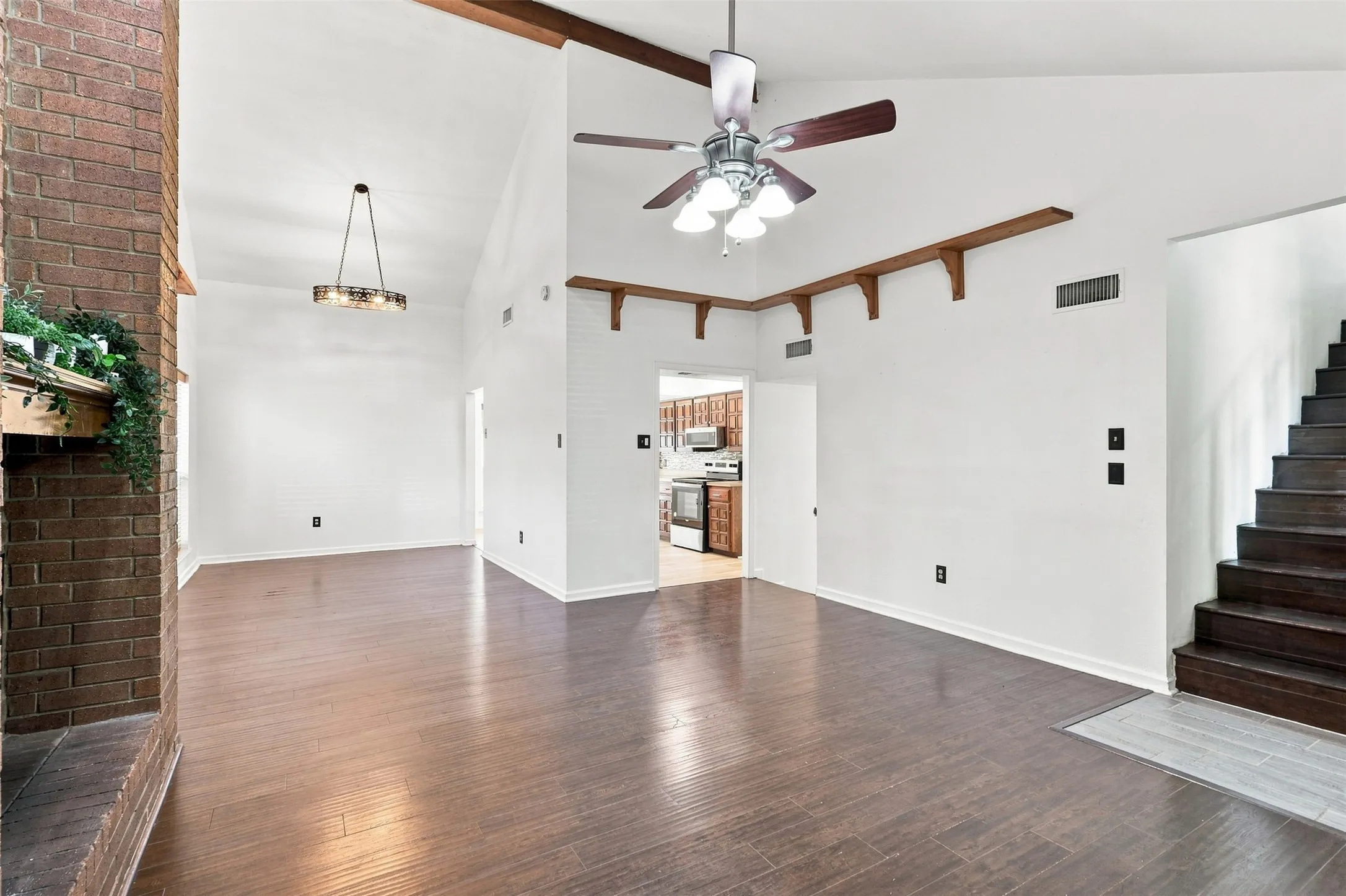 Varnished wood-finish flooring, vaulted ceilings with exposed wood beams, and a brick fireplace