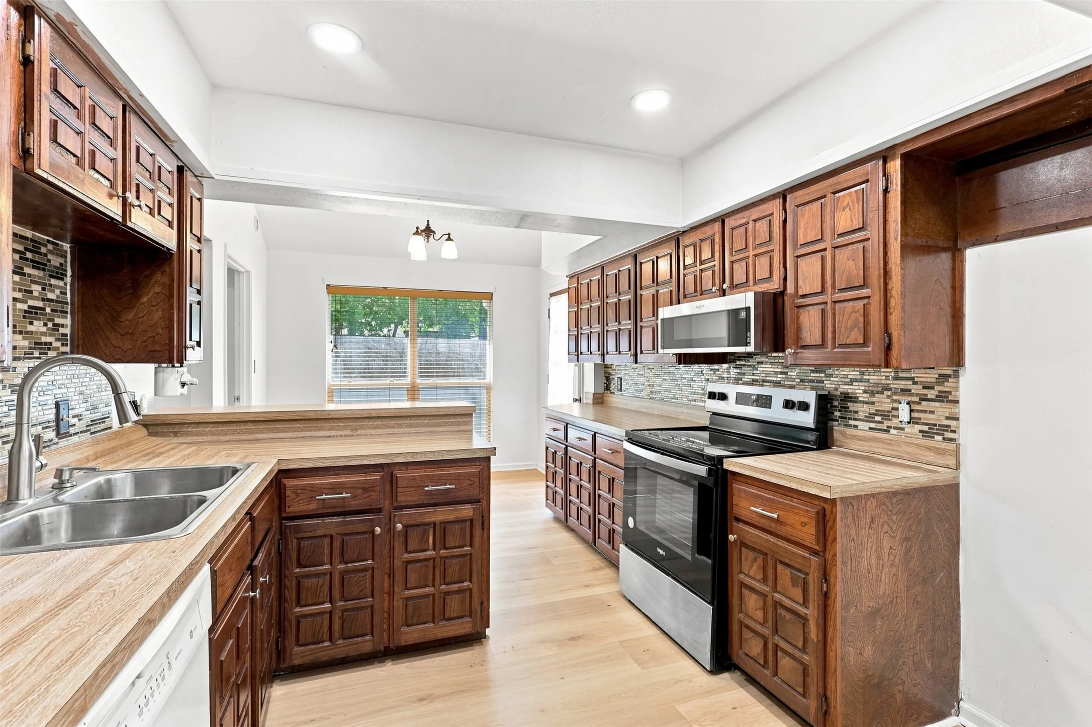 Kitchen featuring wood-finish flooring, two-tone cabinetry, mosaic tile backsplash, stainless steel appliances, and recessed lighting