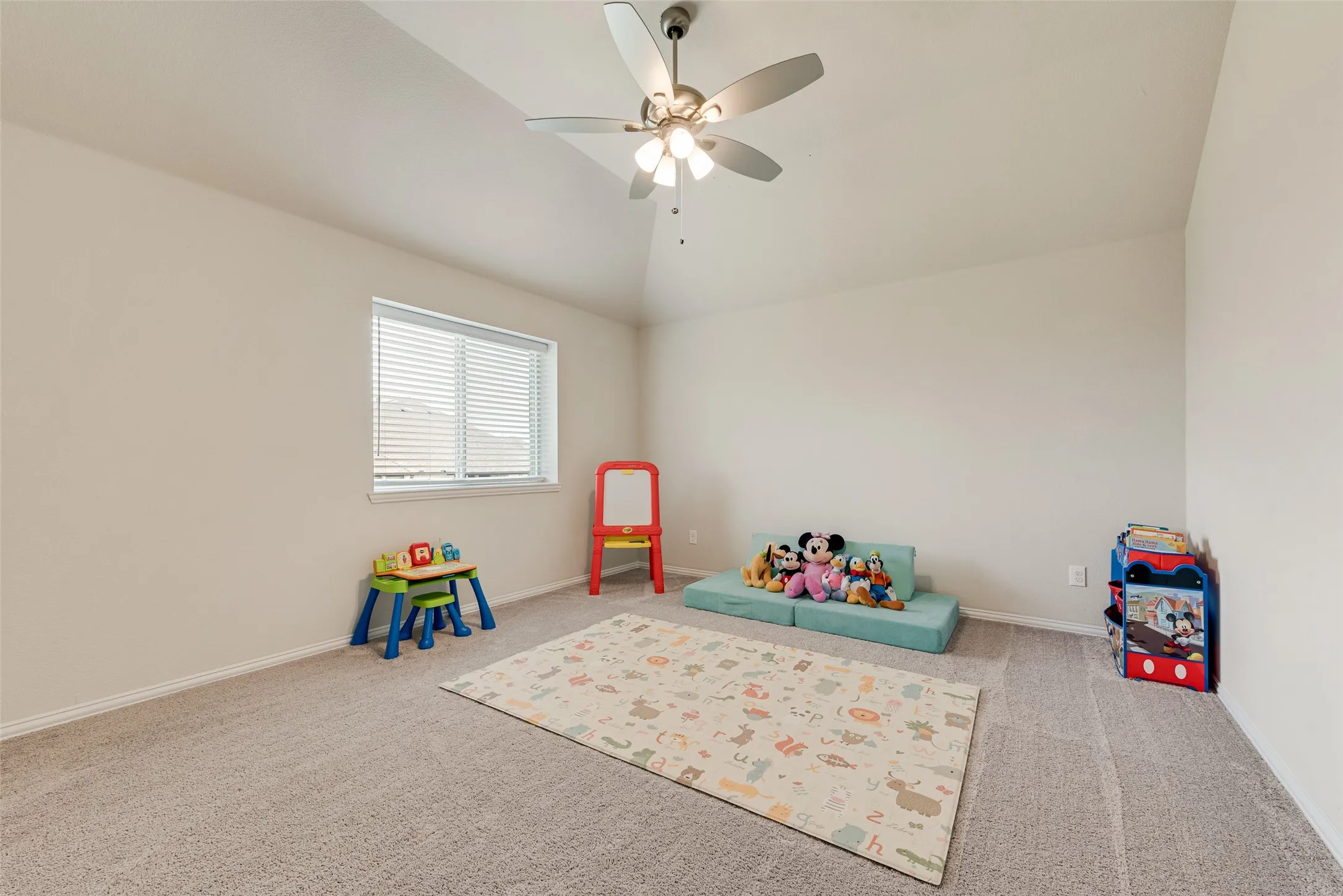Vaulted ceiling with an attached ceiling fan, large window with blinds, light-toned carpeting, and neutral wall paint