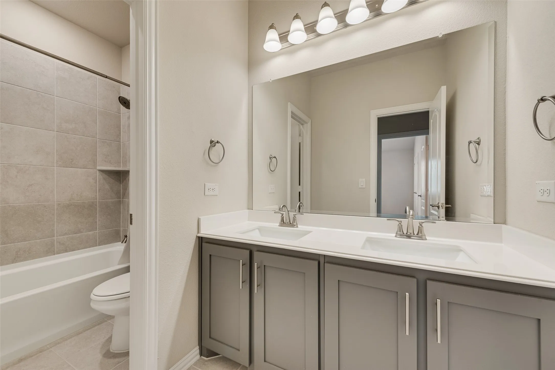 Bathroom featuring a dual vanity with grey cabinetry and white countertops, a large vanity mirror, and a five-bulb light fixture