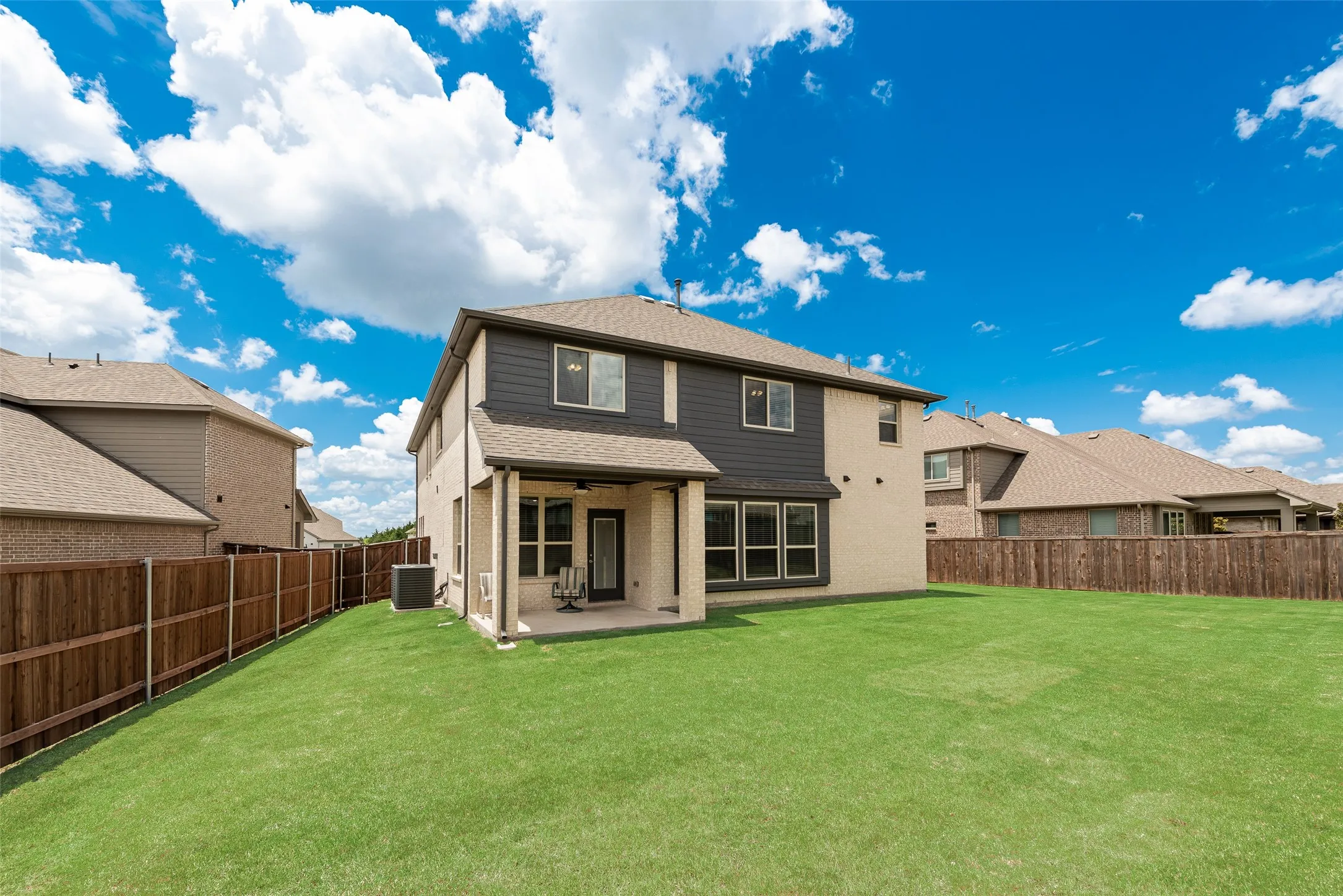 Expansive green lawn with a newly constructed two-story home featuring a brick and siding exterior
