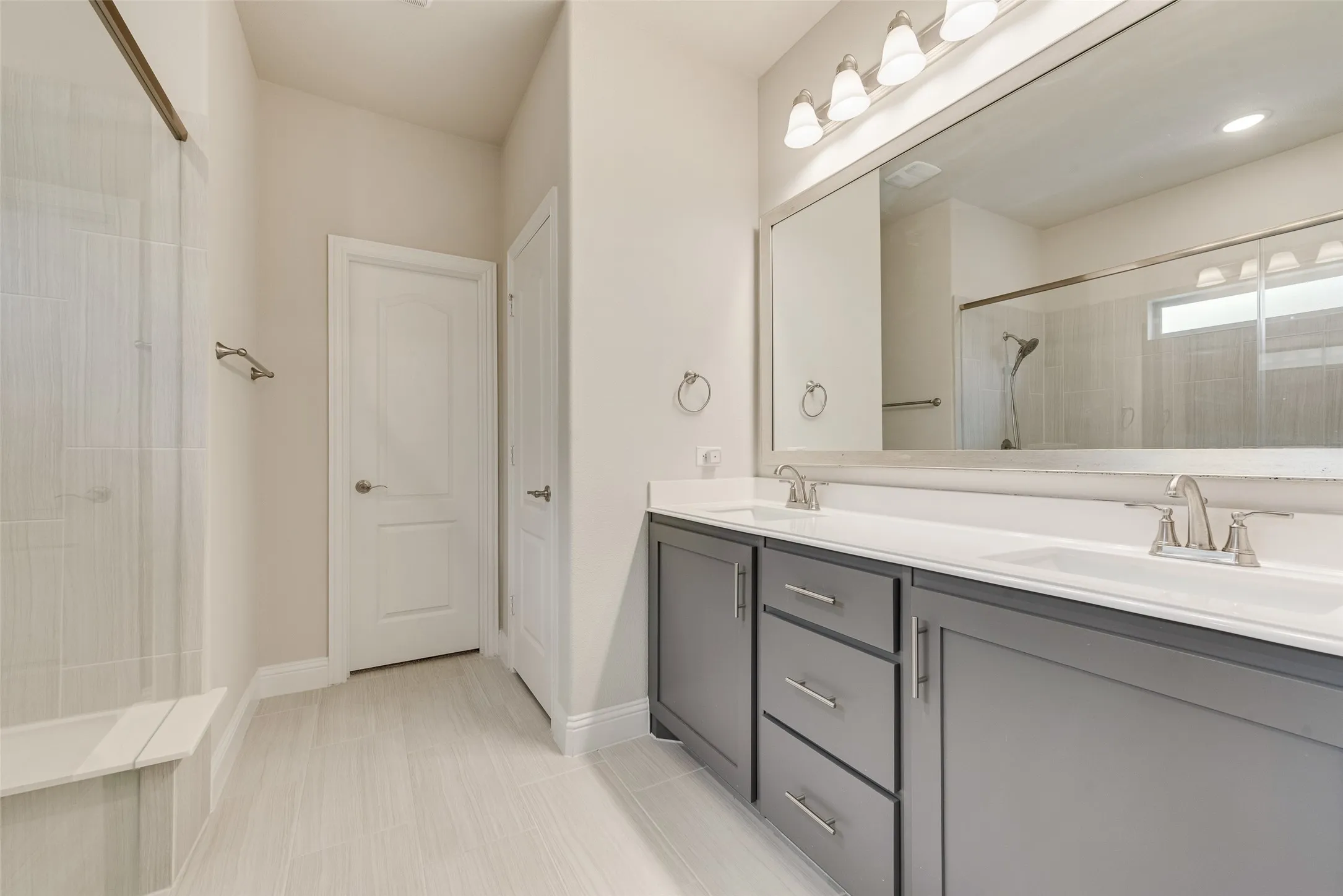 Double vanity with gray cabinetry and white countertops, featuring two undermount sinks and brushed nickel fixtures