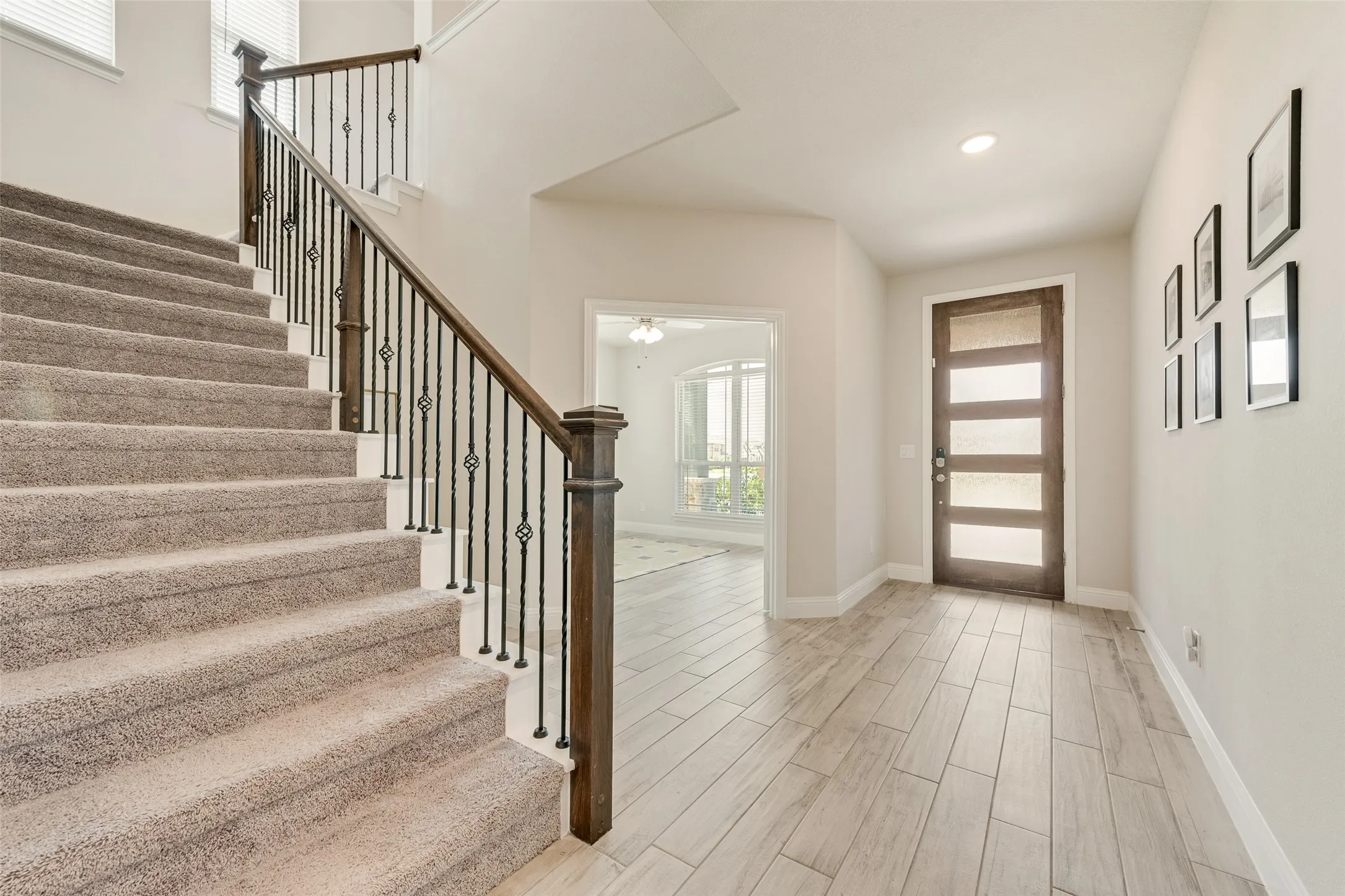 Entryway featuring wood-look tile flooring, a dark wood entry door with frosted glass panels, and a carpeted staircase with a dark wood handrail and wrought iron balusters