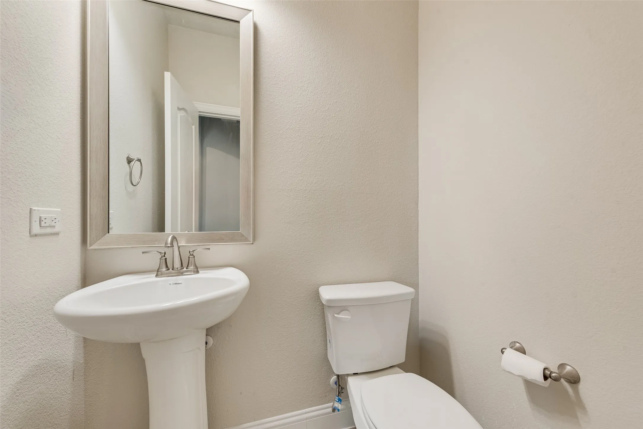 Pedestal sink with a brushed nickel faucet, framed mirror, and a white toilet