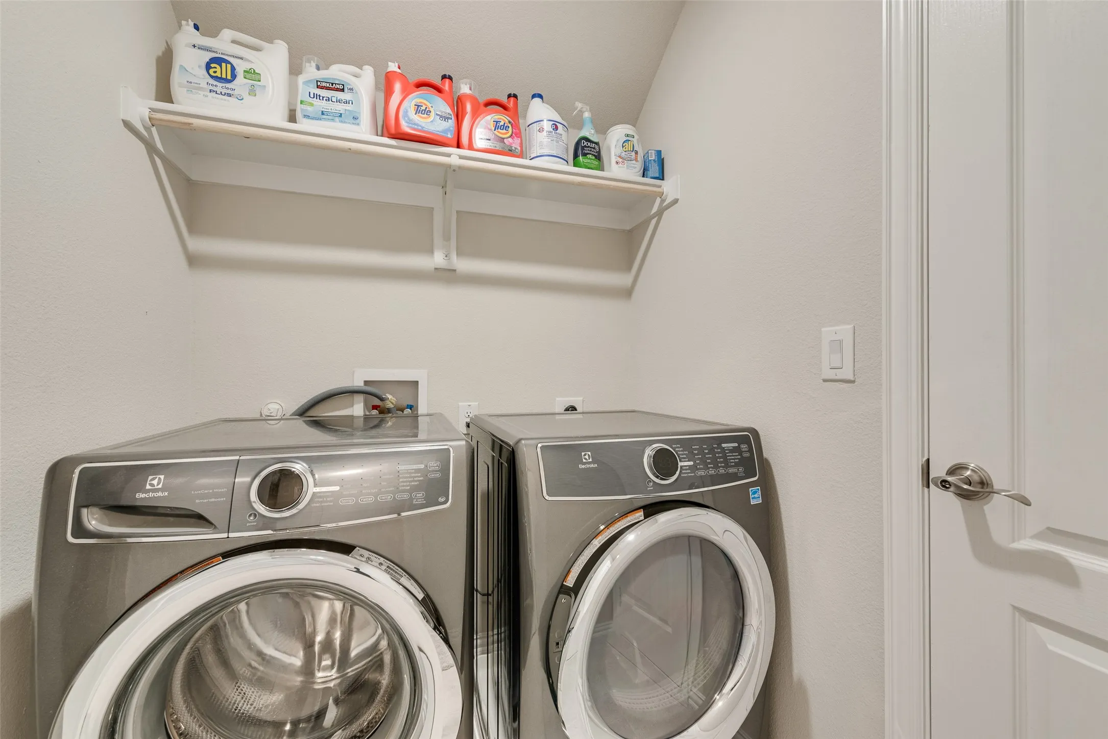 Dedicated laundry area featuring a white wall shelf, light gray wall paint, and a white interior door with brushed nickel hardware