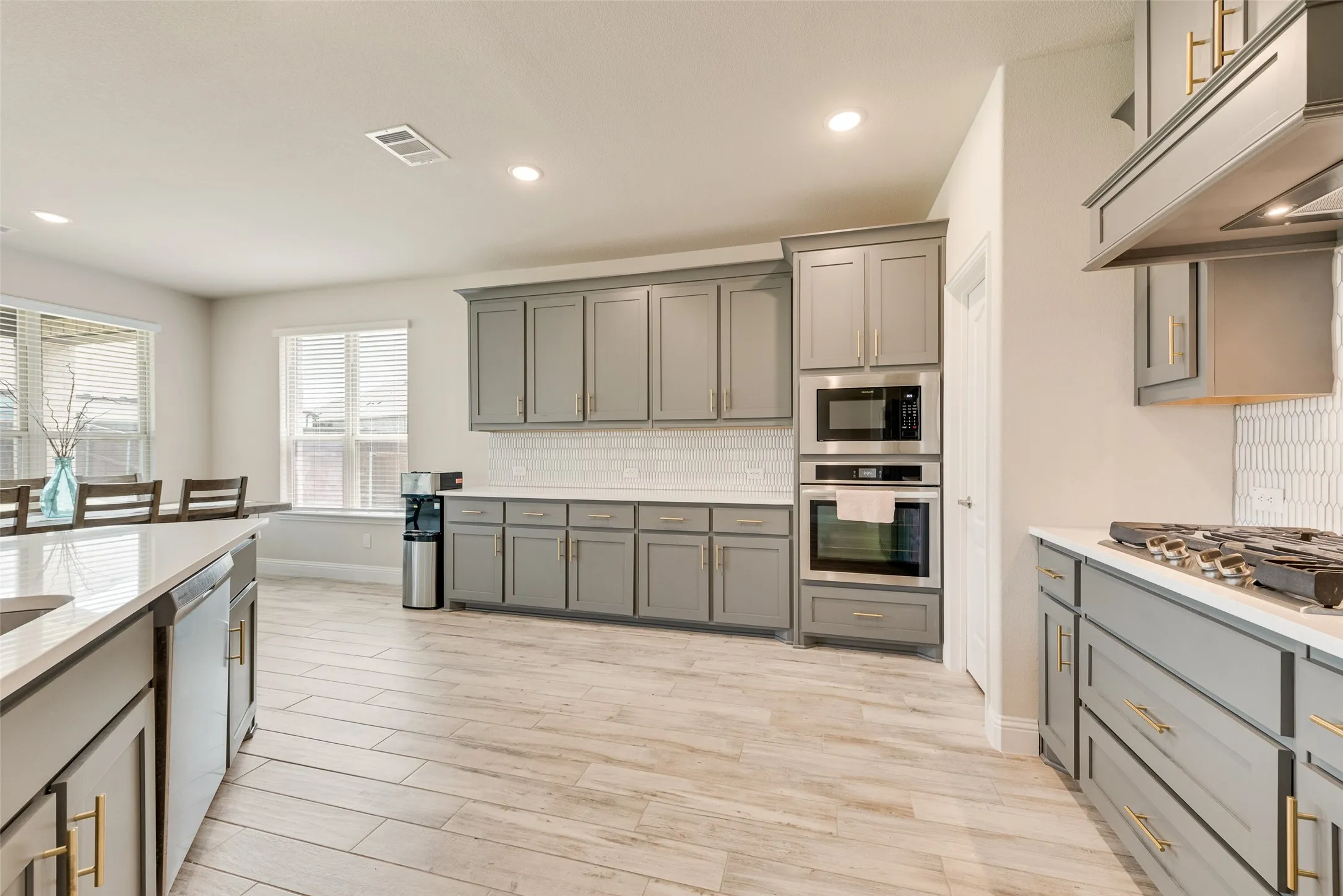 Open-concept kitchen featuring extensive grey cabinetry, light-toned countertops, a built-in oven and microwave, a gas cooktop, and wood-finish flooring