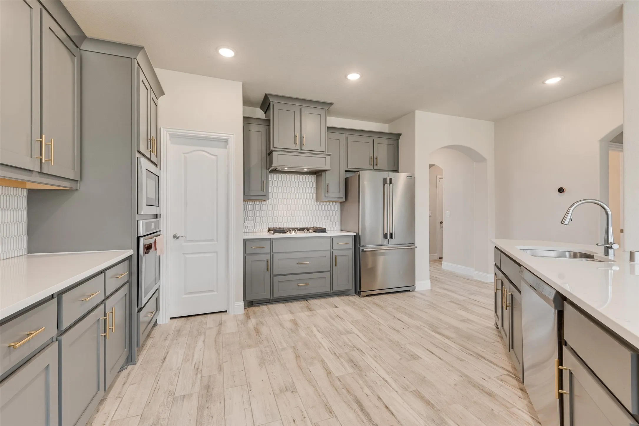 Spacious kitchen featuring gray cabinetry, gold-tone hardware, stainless steel appliances, white countertops, and wood-finish flooring