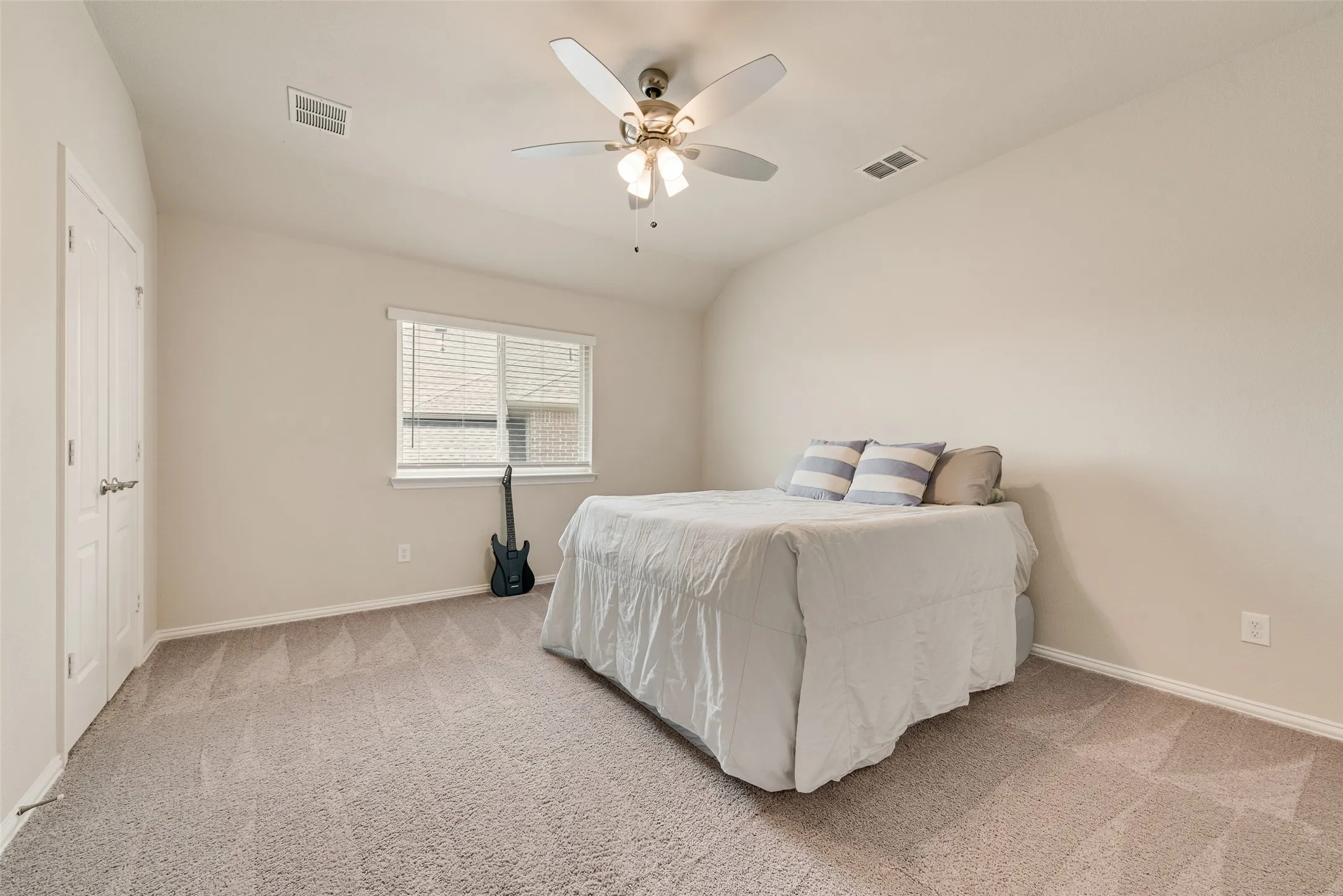 Room featuring light neutral wall paint, patterned carpet flooring, a window with horizontal blinds, a white ceiling fan with integrated lighting, and a bi-fold closet door