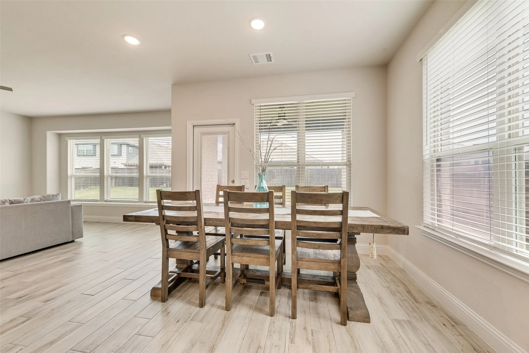Open-concept dining area featuring light wood-finish flooring, recessed lighting, and multiple windows with blinds