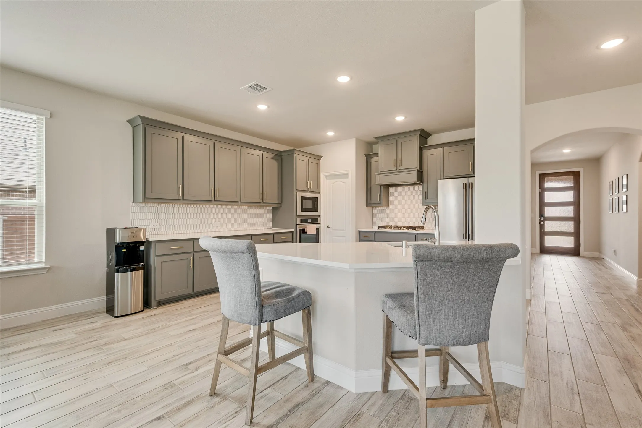 Modern kitchen featuring a large island with white countertop, grey cabinetry, white subway tile backsplash, stainless steel appliances, and wood-finish flooring