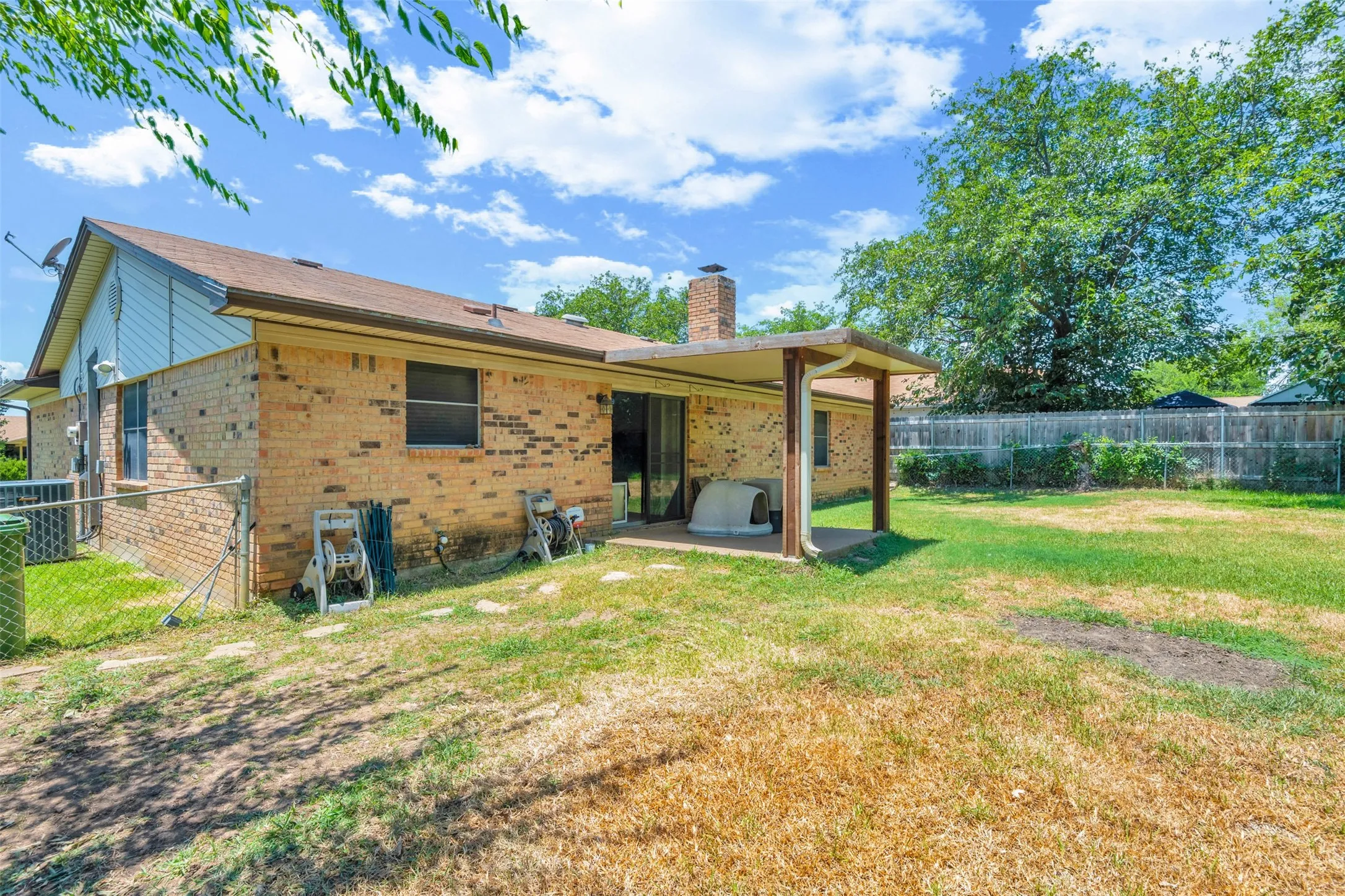 Expansive backyard featuring a covered patio, brick exterior, and a chain-link fence