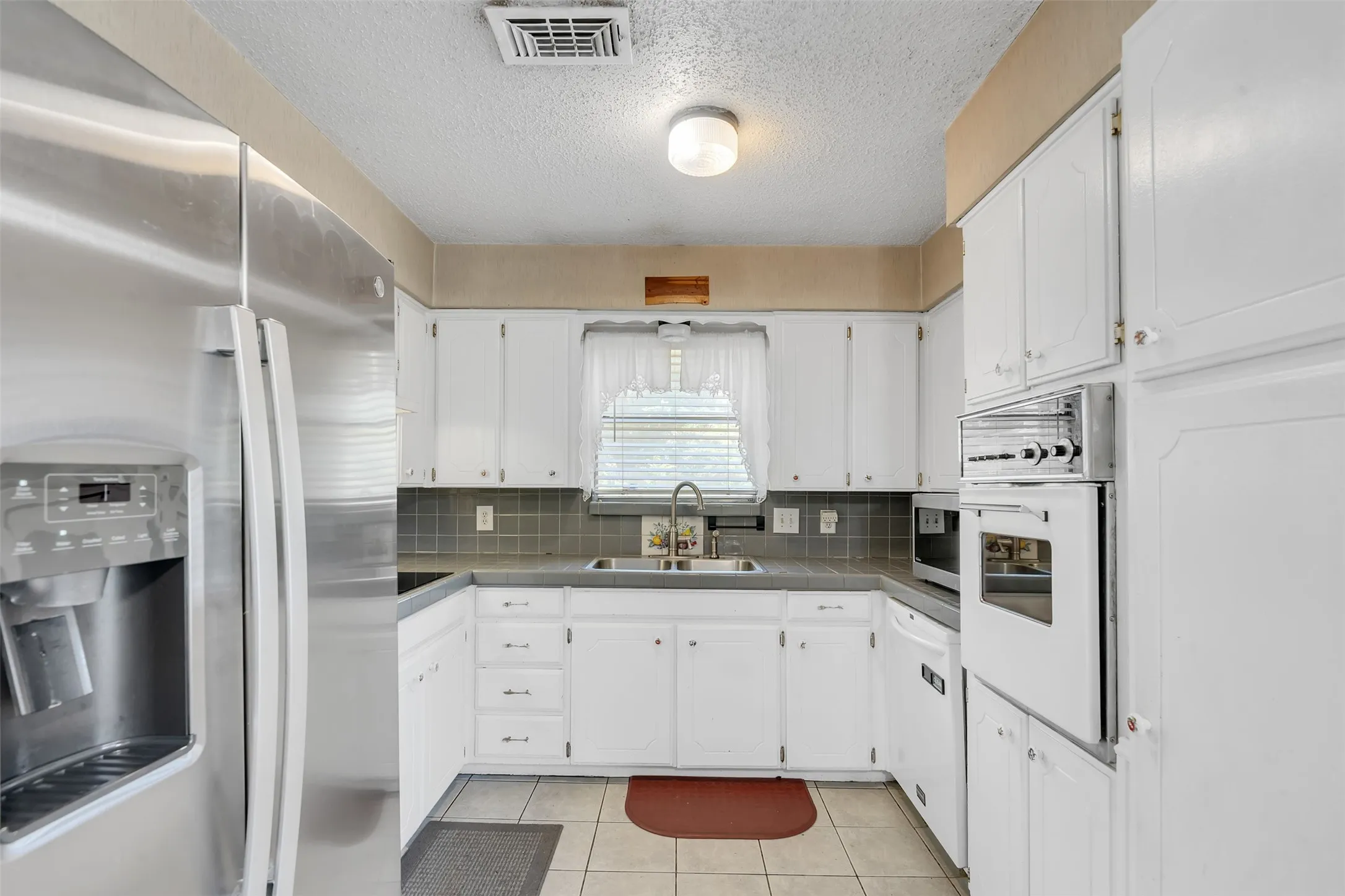 Kitchen featuring white cabinetry, a built-in oven, stainless steel refrigerator, tile backsplash, and a double basin sink
