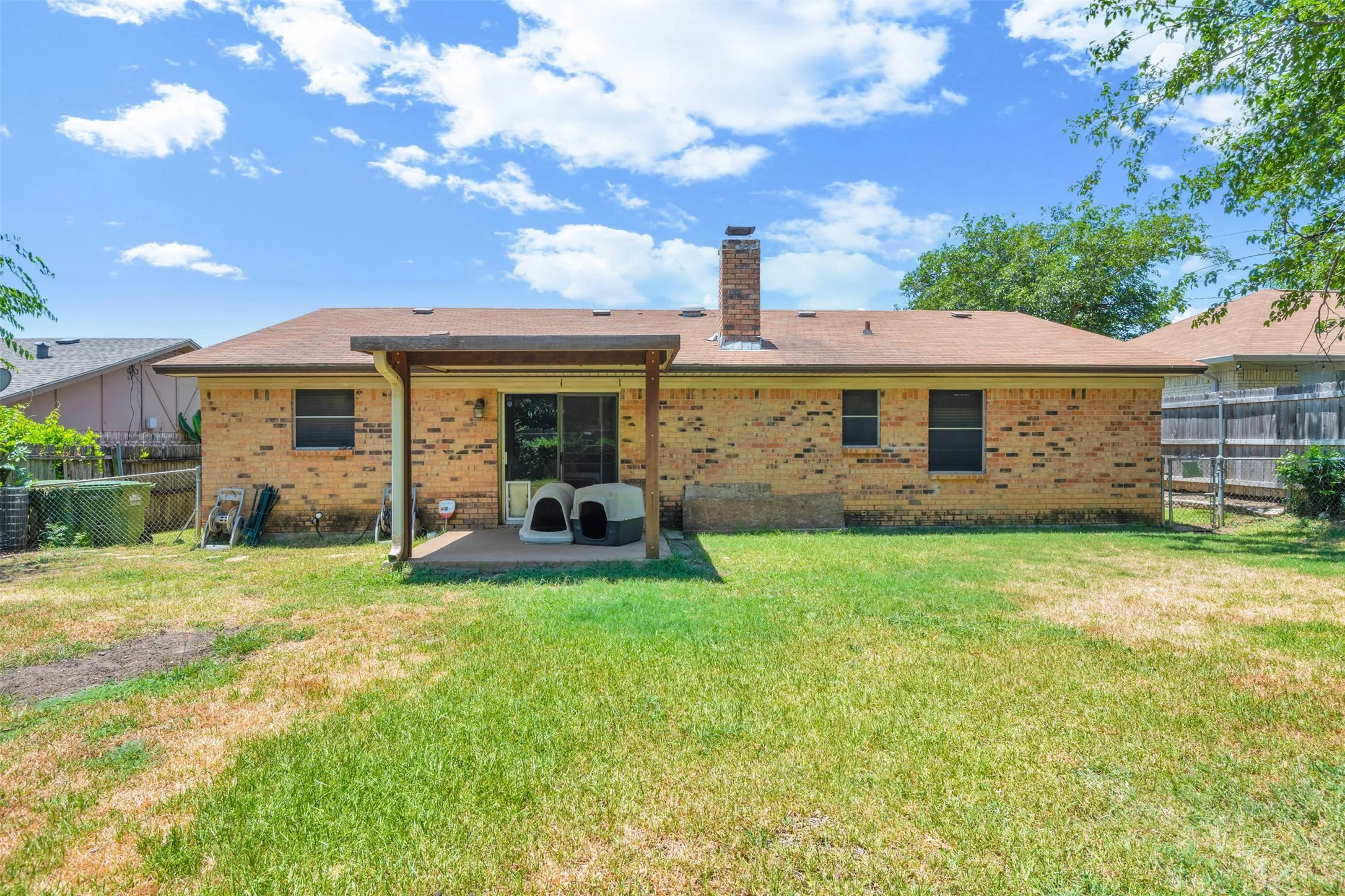 Expansive backyard featuring a covered patio, brick exterior, and a prominent chimney
