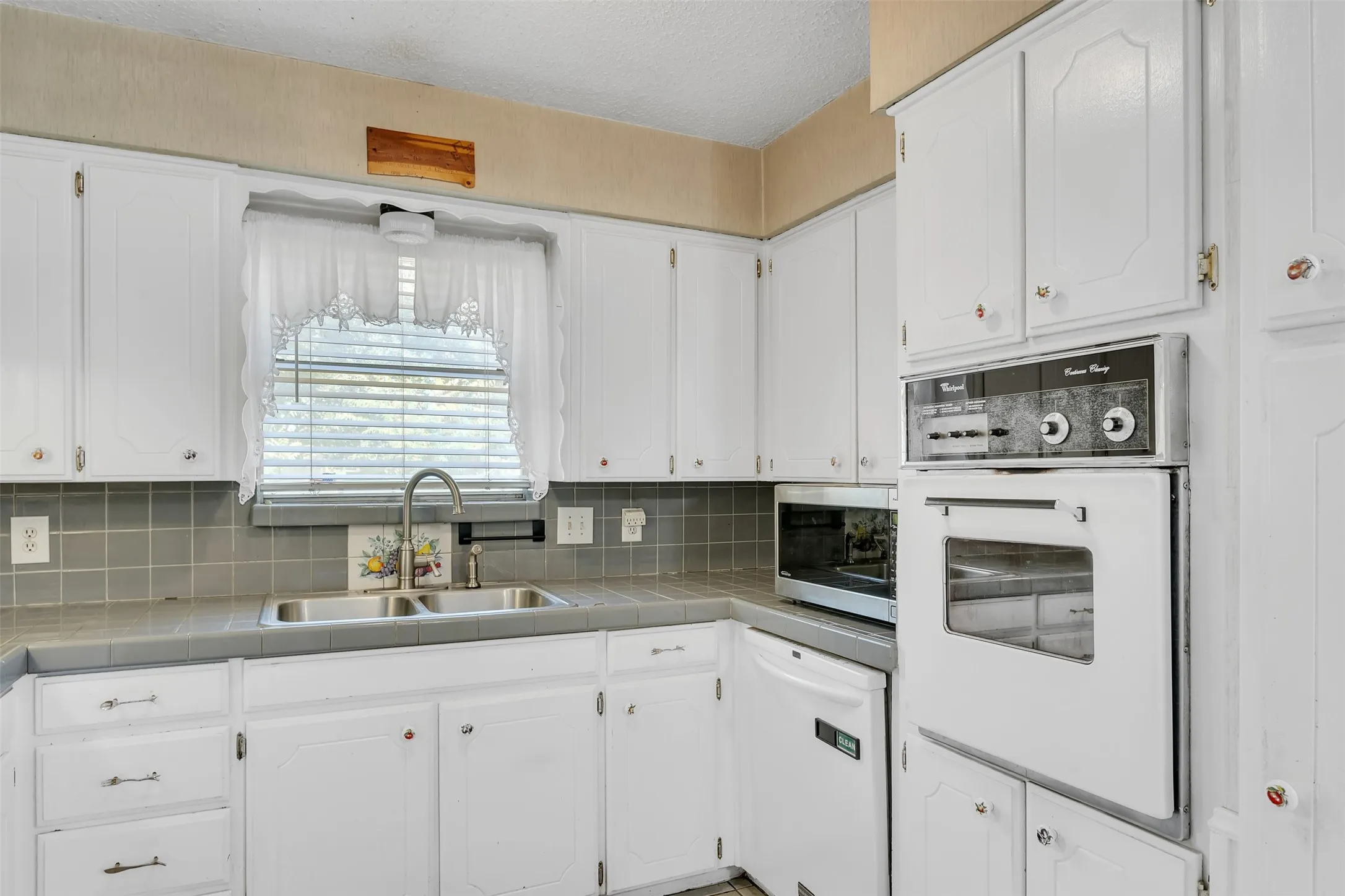 Kitchen featuring white cabinetry, a double basin stainless steel sink with a gooseneck faucet, a light gray tiled backsplash, and built-in appliances