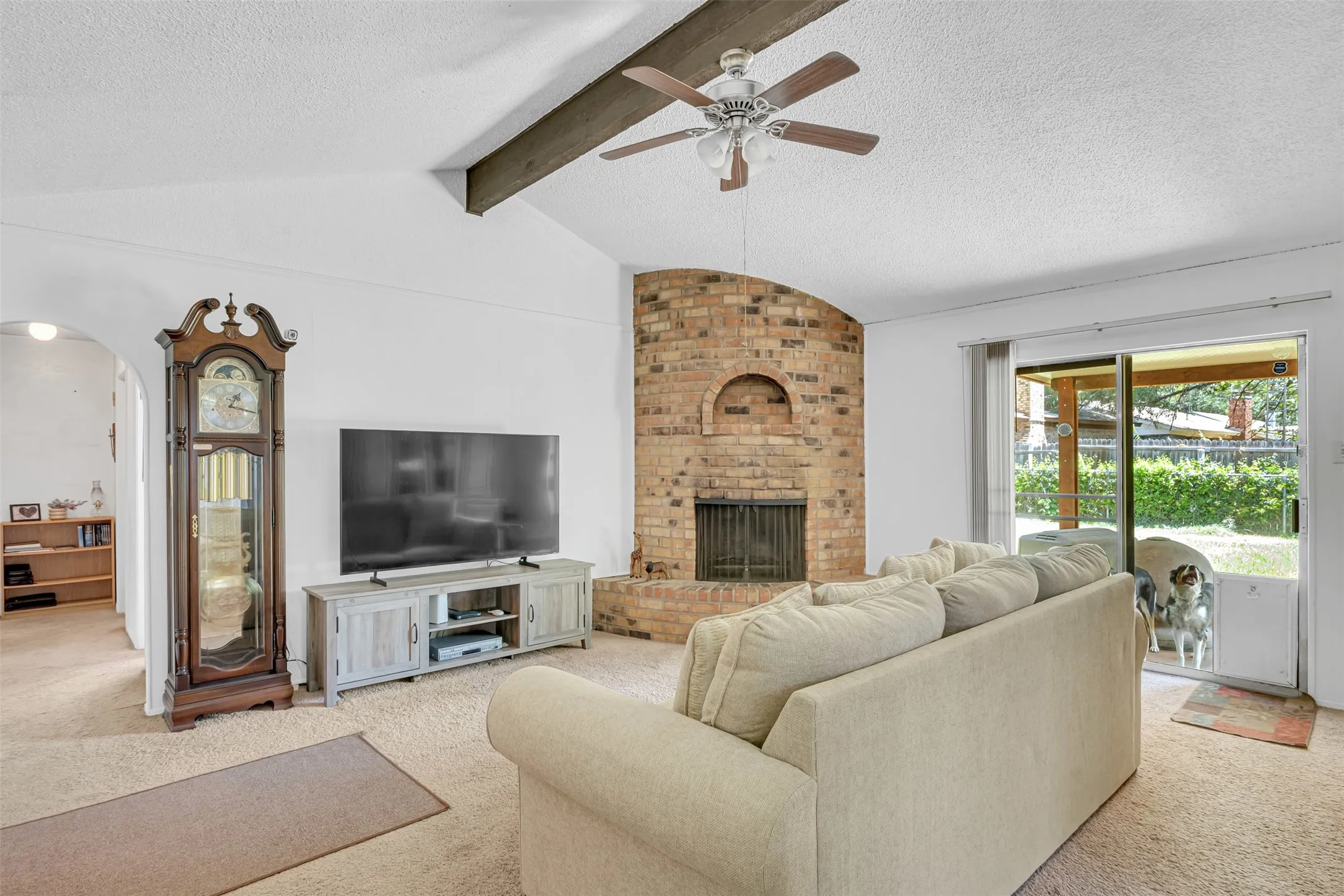 Living area featuring a vaulted ceiling with exposed beam, a ceiling fan, and a brick fireplace