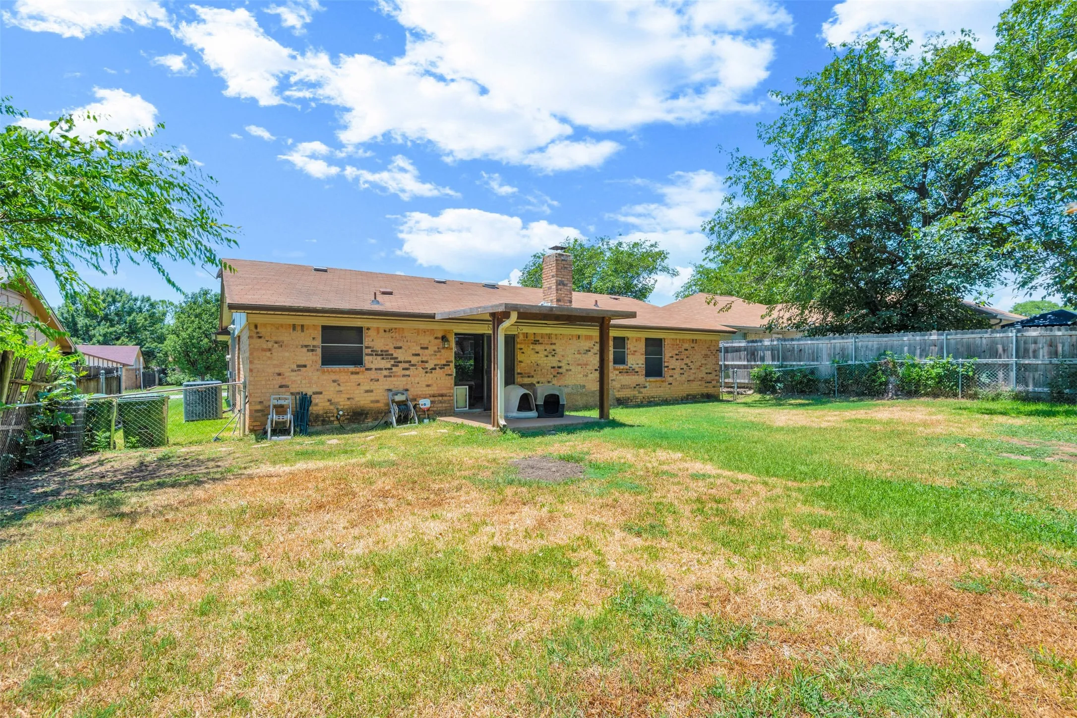 Spacious backyard featuring a covered patio, brick exterior, and mature perimeter trees