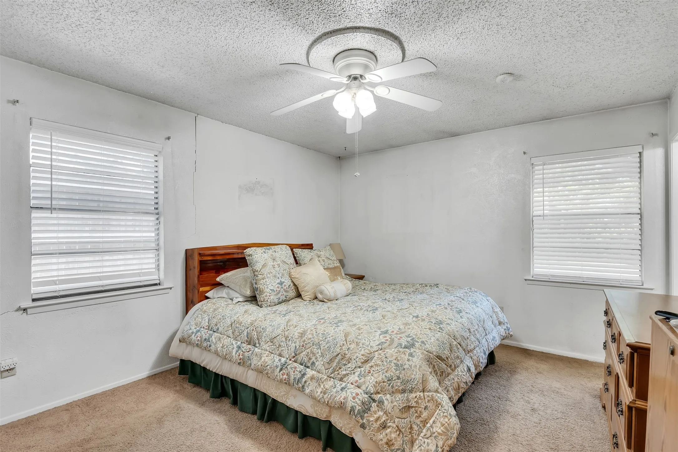 Bedroom featuring a ceiling fan with light fixture, two windows with blinds, and carpet flooring
