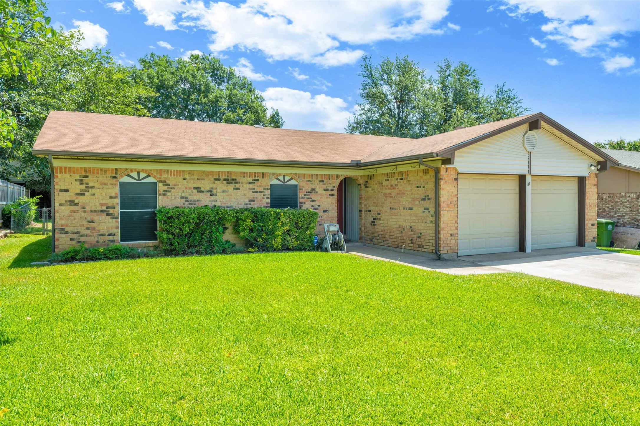 Brick exterior featuring a two-car garage, established front lawn, and mature landscaping