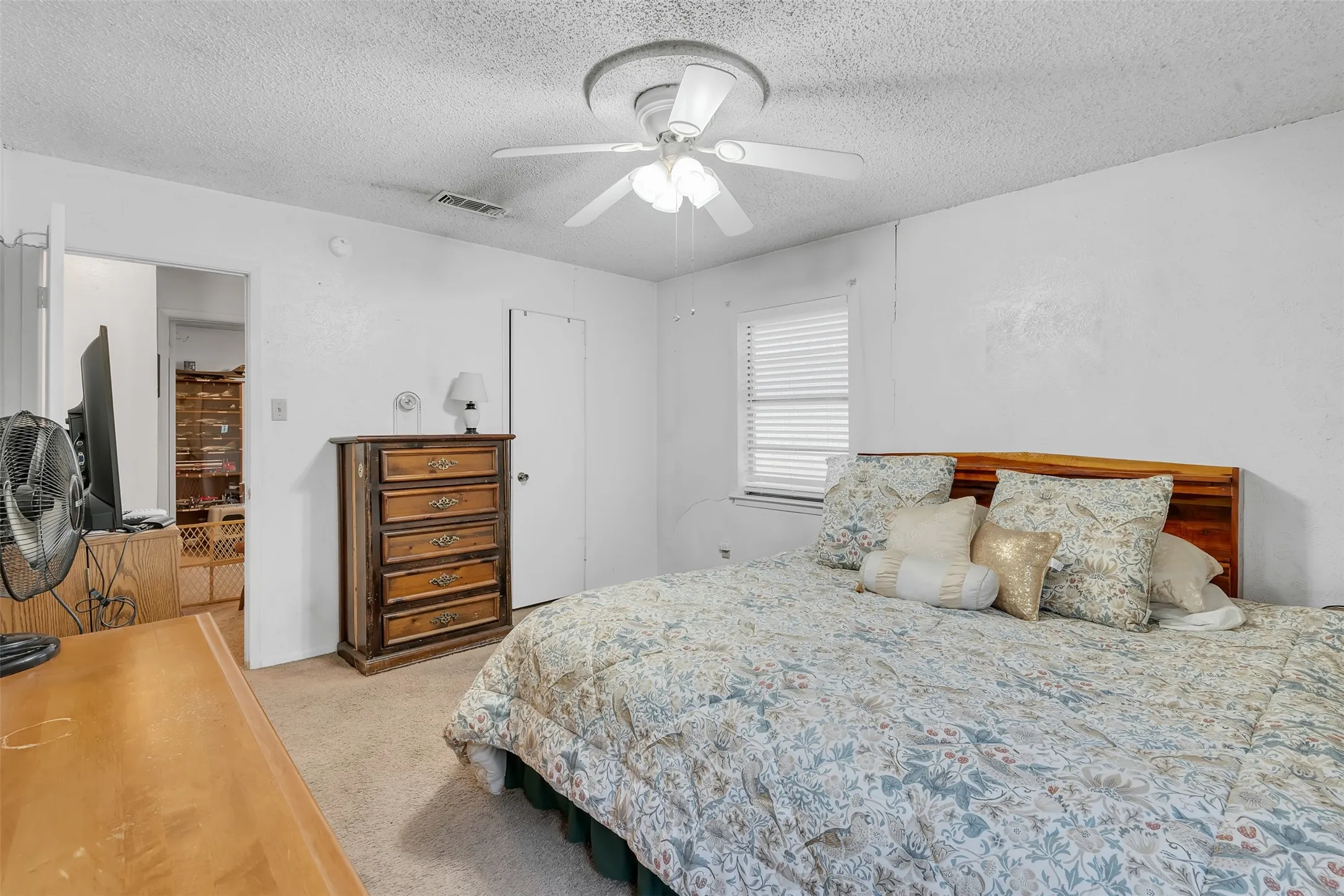 Carpeted room featuring a ceiling fan with integrated lighting, a window with horizontal blinds, a wood-finish headboard, and white painted walls